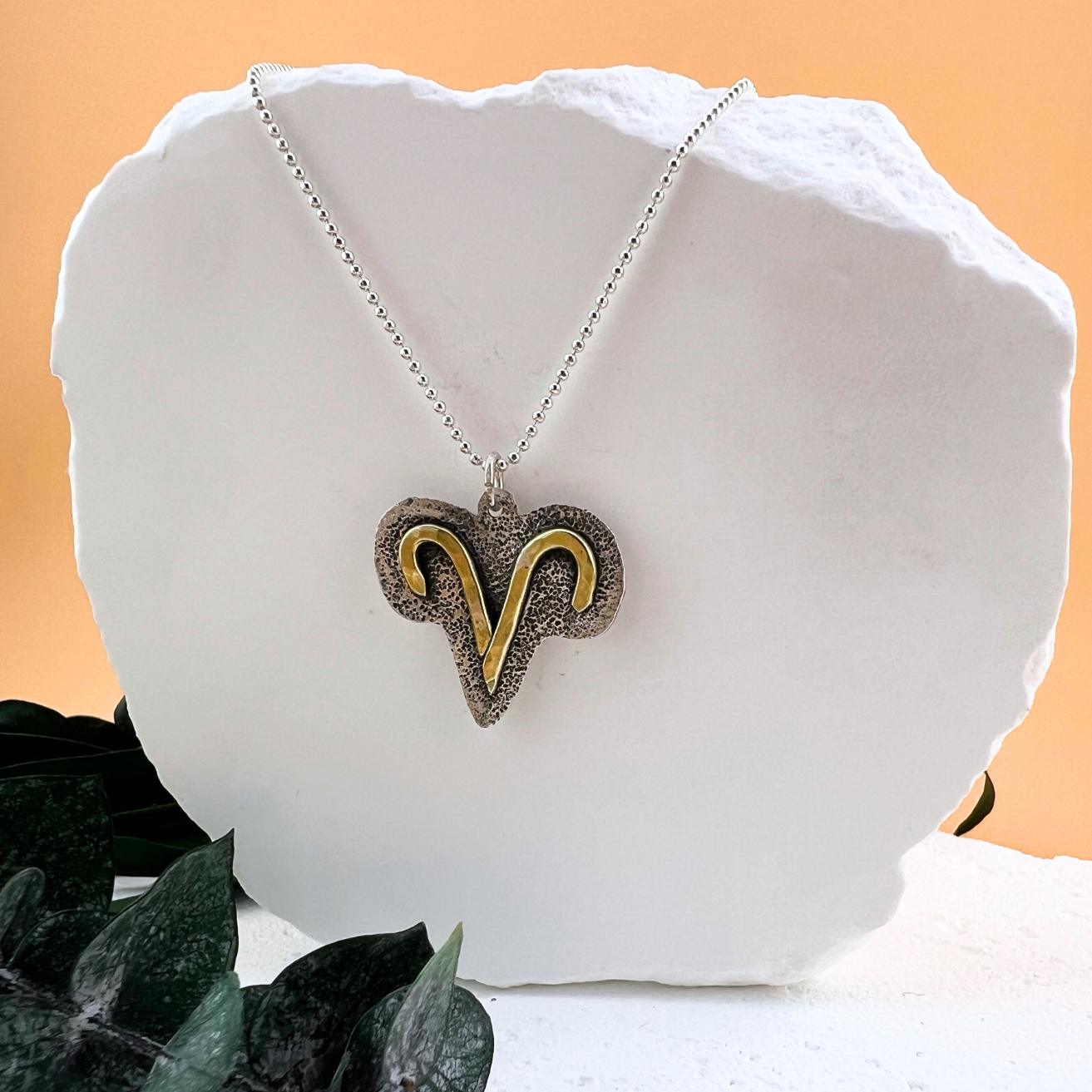 Aries zodiac necklace with brass symbol on textured sterling silver pendant.
