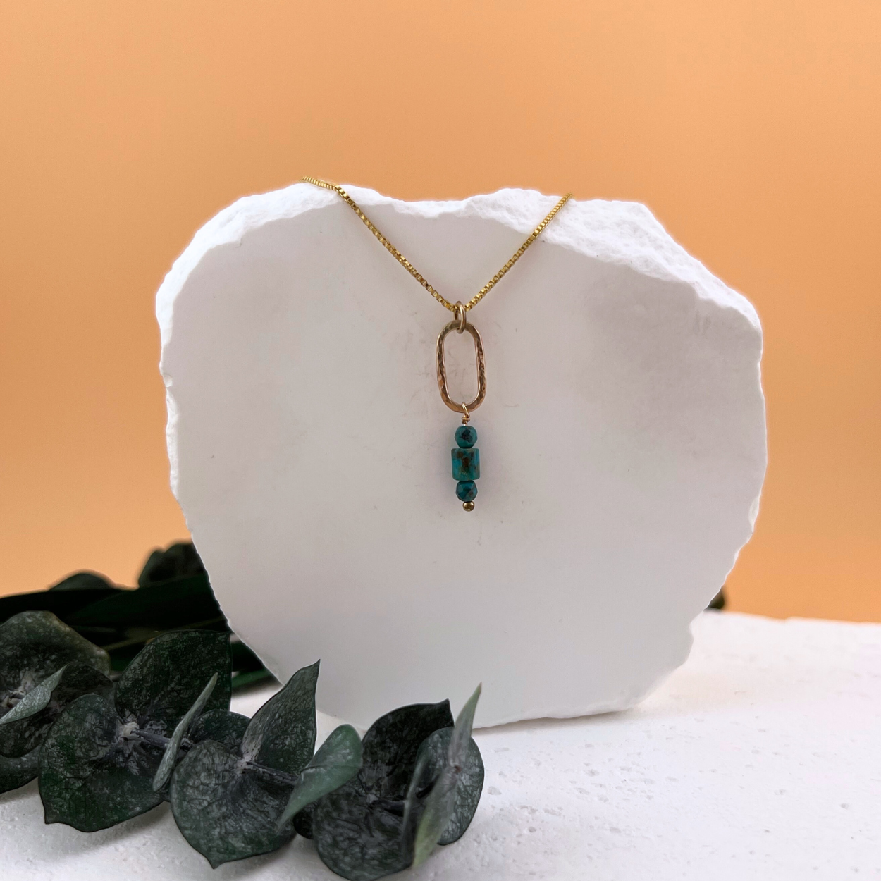 Anchor + Sky Necklace in 14kt gold fill featuring a hammered oval link with Kingman turquoise beads, displayed on a white stone backdrop.