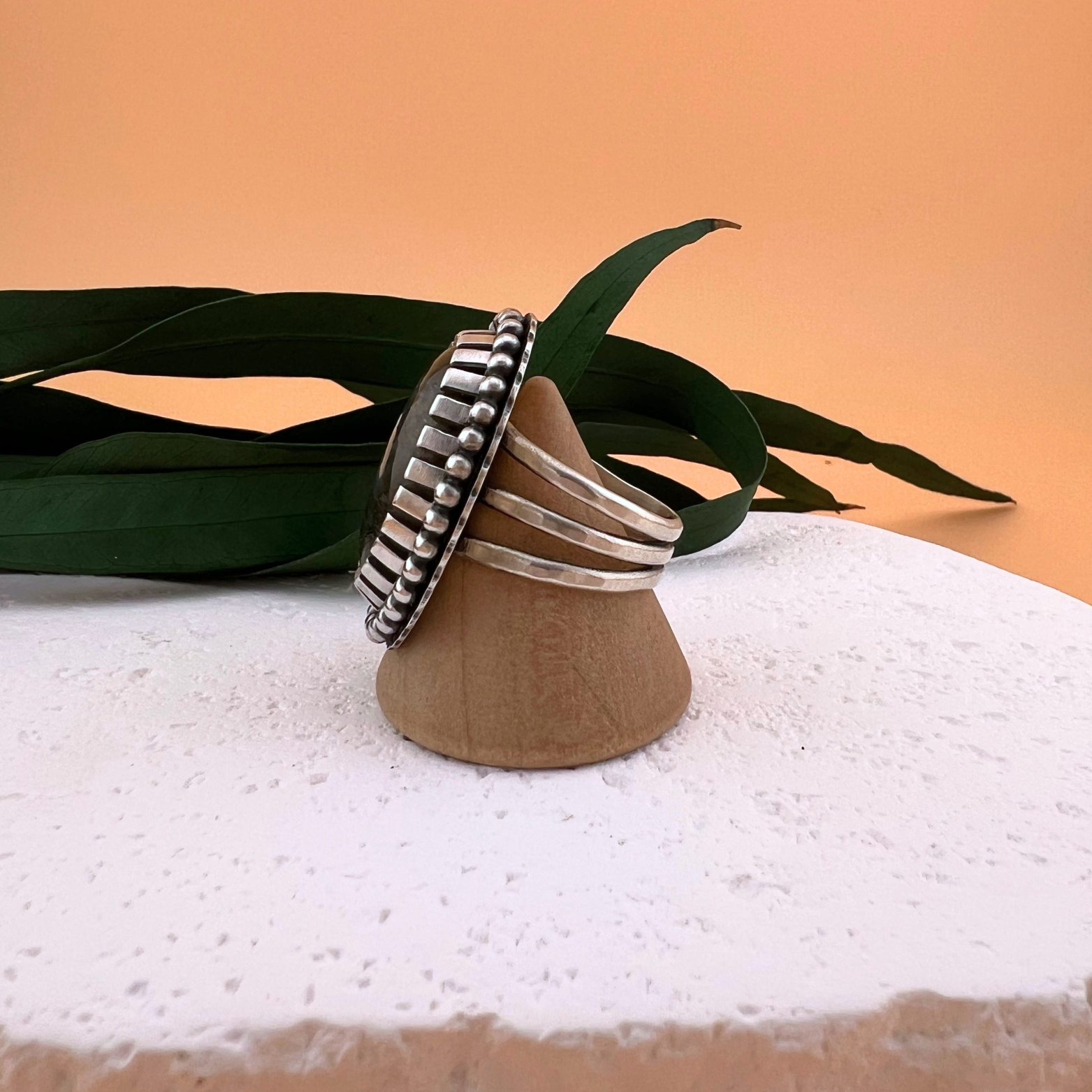 Side profile of a labradorite ring in sterling silver on a wooden ring stand, showing the handcrafted bezel and decorative silver detailing.