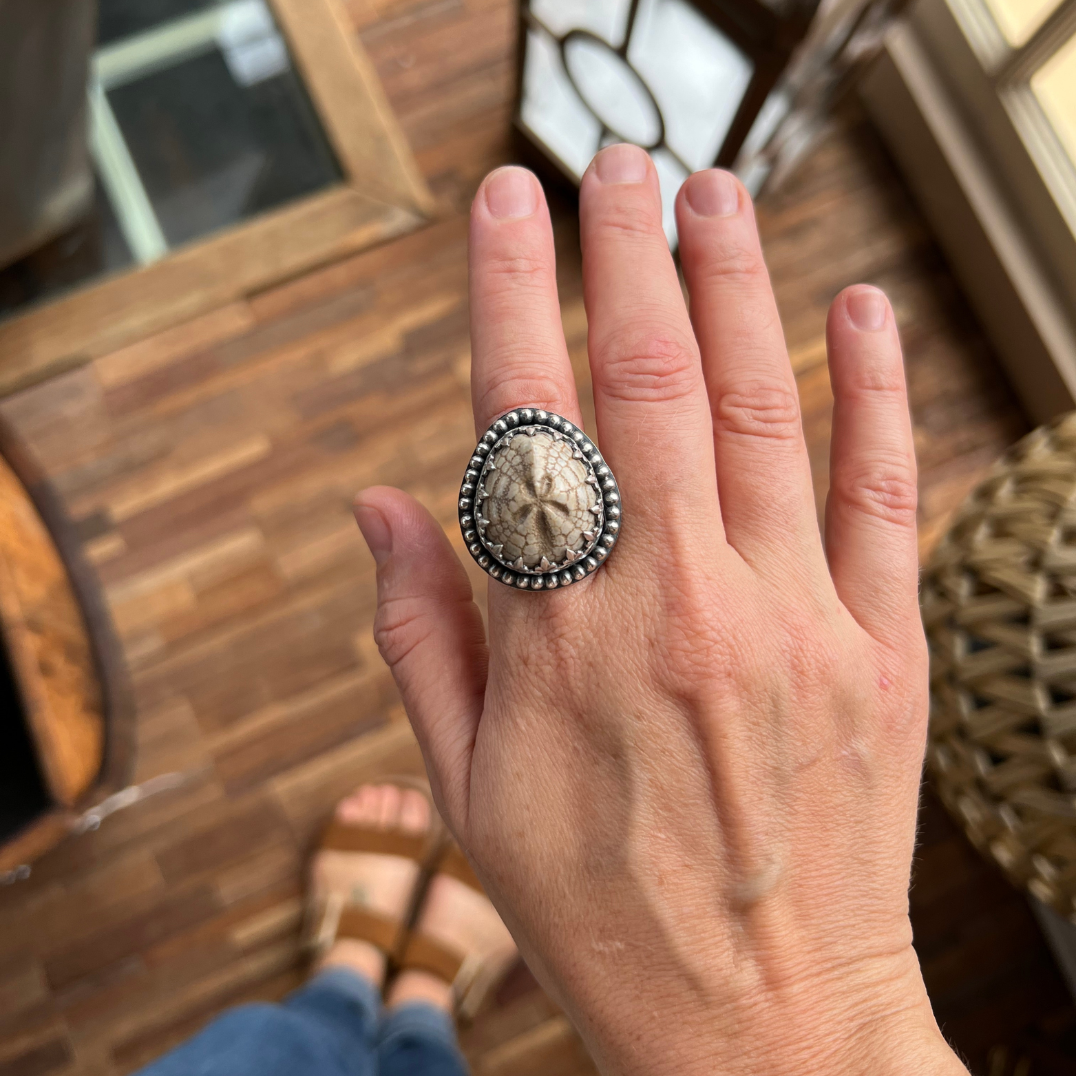 Fossilized sea urchin sterling silver ring worn on a hand, showcasing the scale and organic star pattern of the fossil.