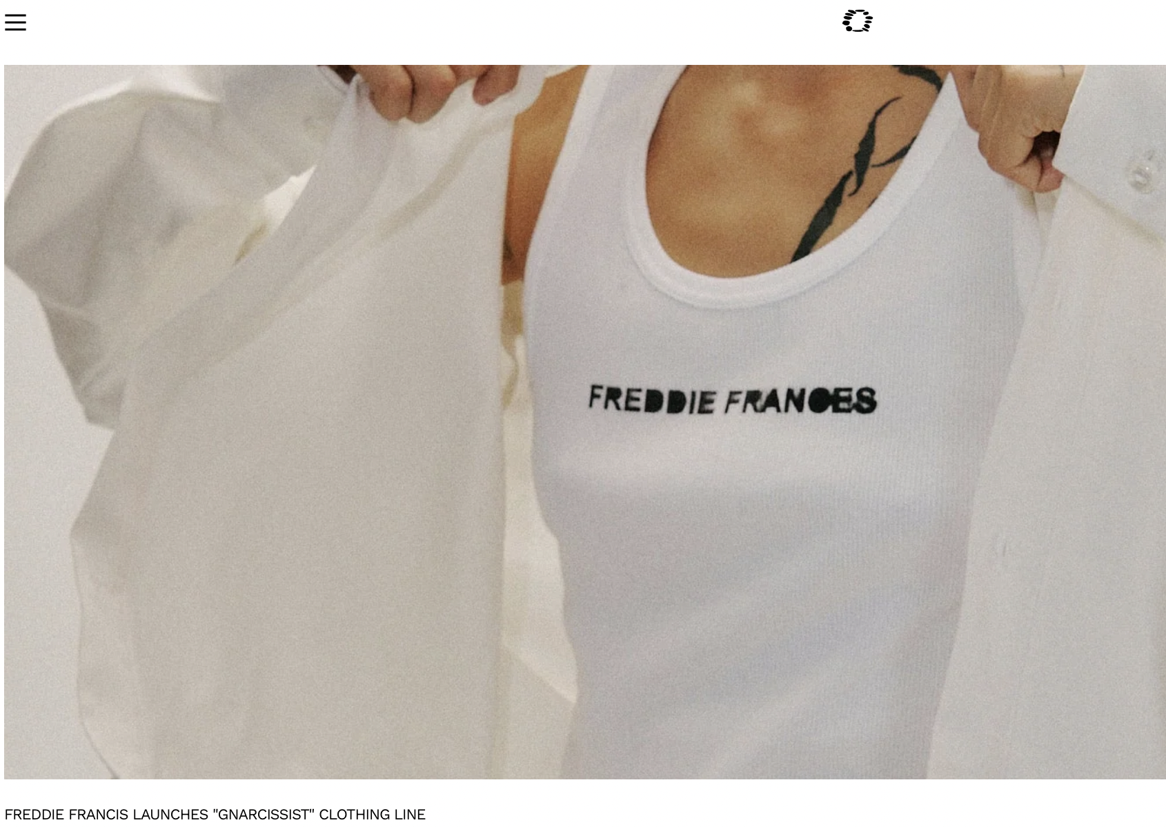 Close-up of a person wearing a white tank top with black text and a white jacket, showing a tattoo on their shoulder.