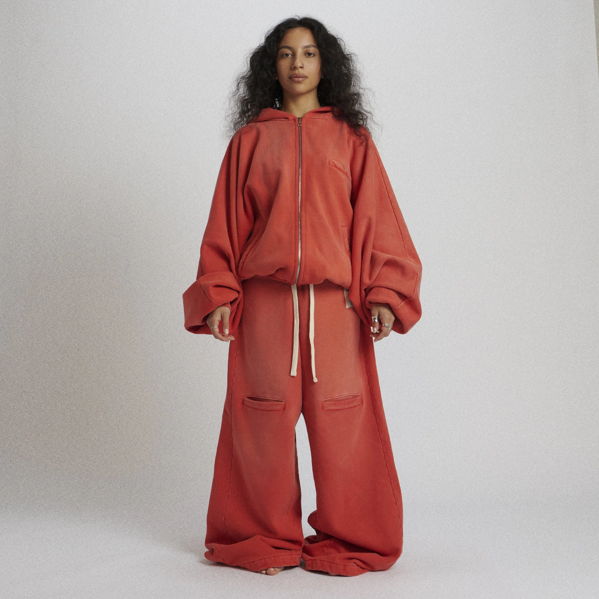 Woman wearing oversized red hoodie and matching wide-leg pants with drawstring waist, standing against a plain gray background.