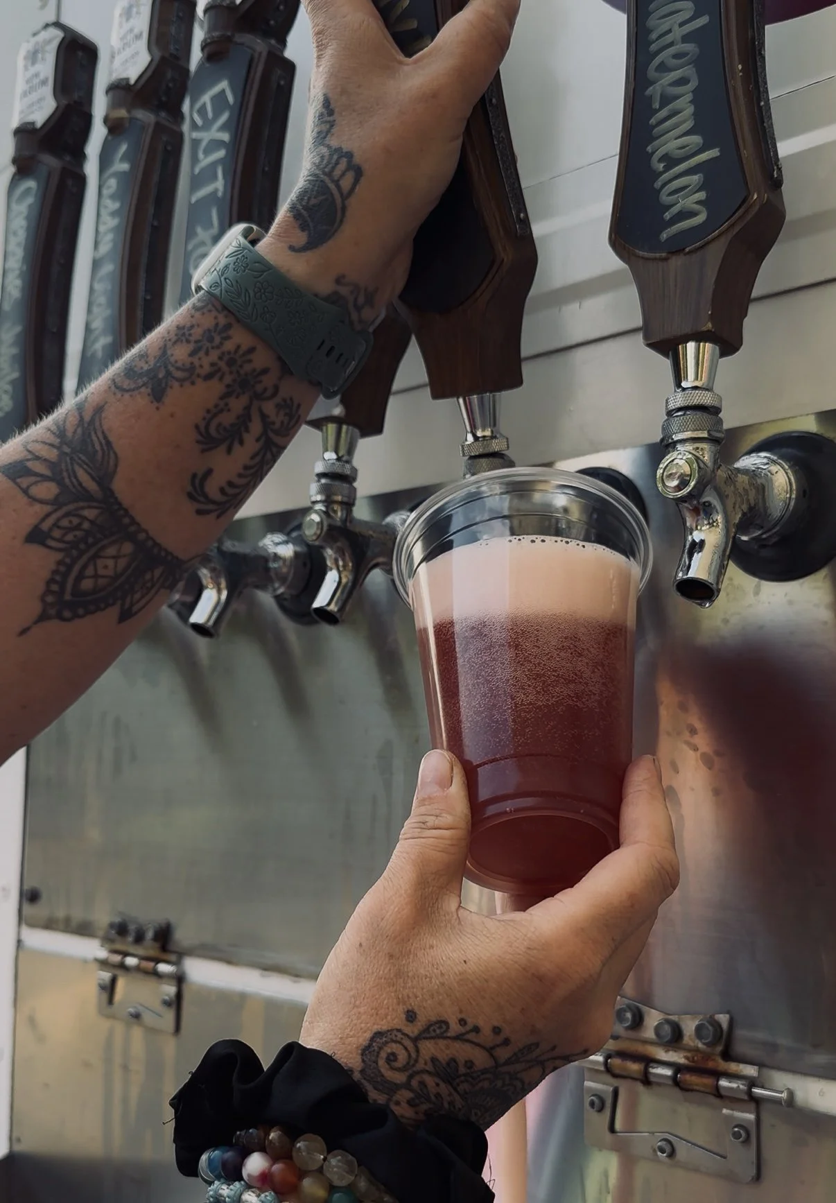 Person filling a clear plastic cup with cold brew coffee from a tap system at a coffee shop.