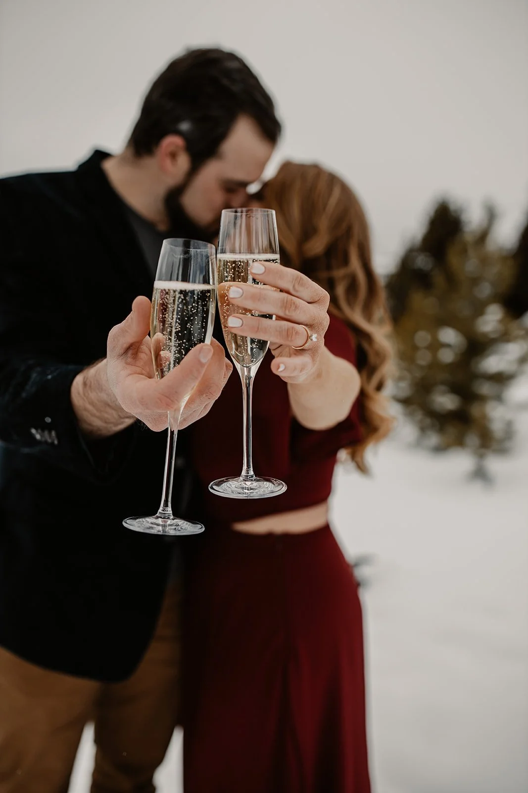 A couple holding champagne glasses in a toast with a snowy outdoor background.