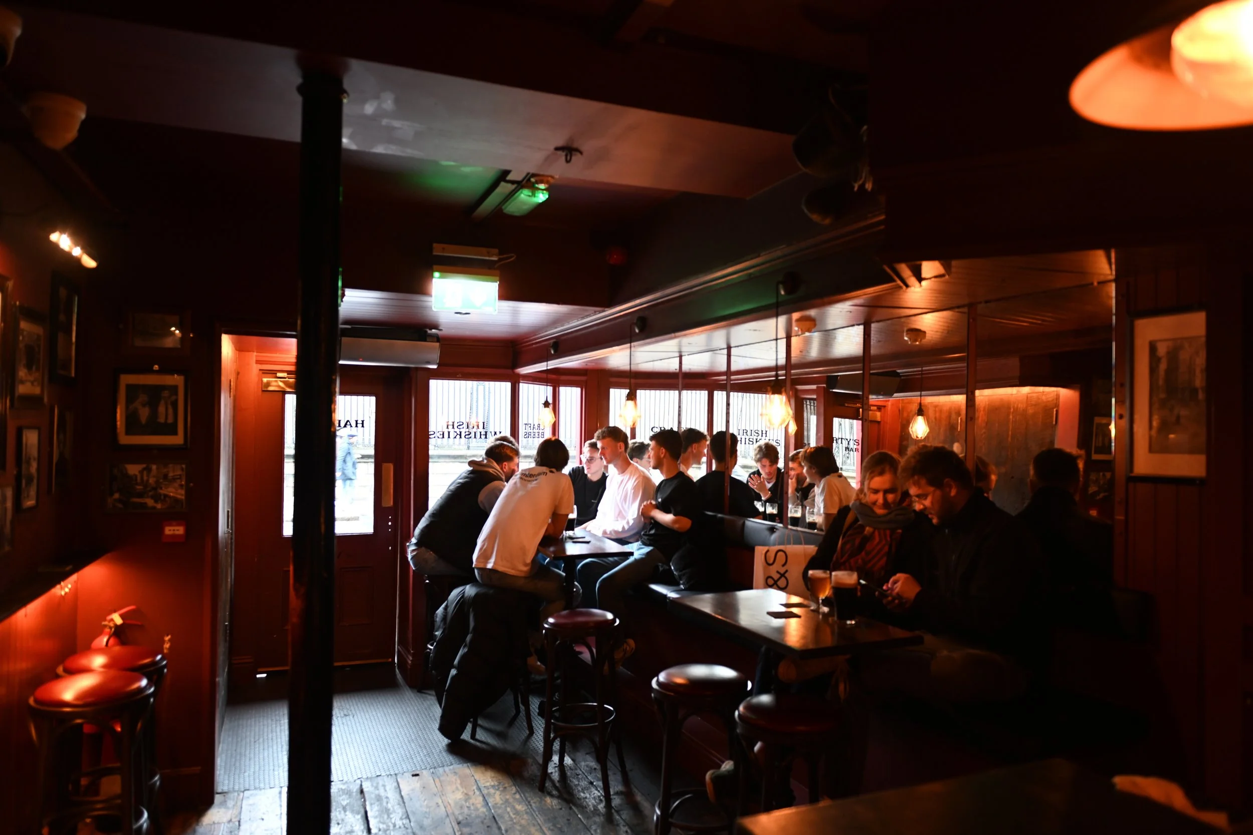People sitting at tables in a dimly lit pub, engaging in conversations and using their phones.