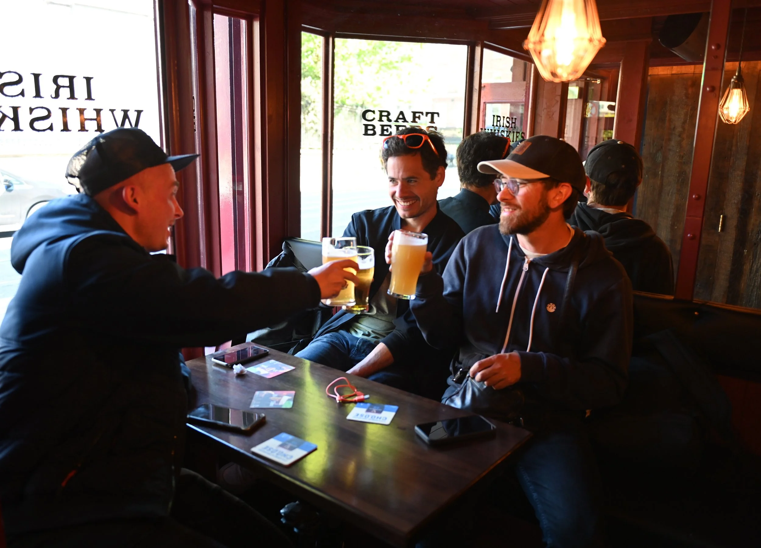 Four friends enjoying drinks at a bar, raising their glasses for a toast, smiling and engaging in conversation.