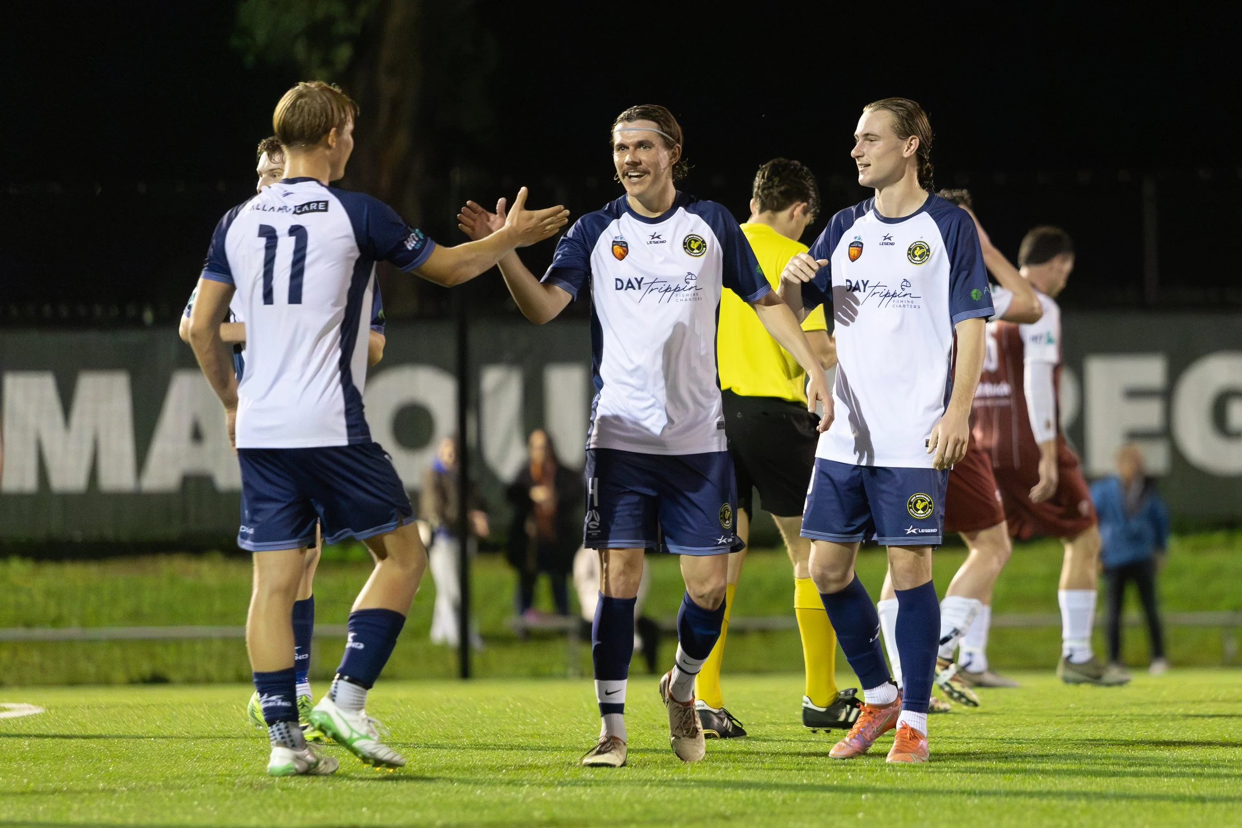 Soccer players in blue and white uniforms celebrating on the field at night.