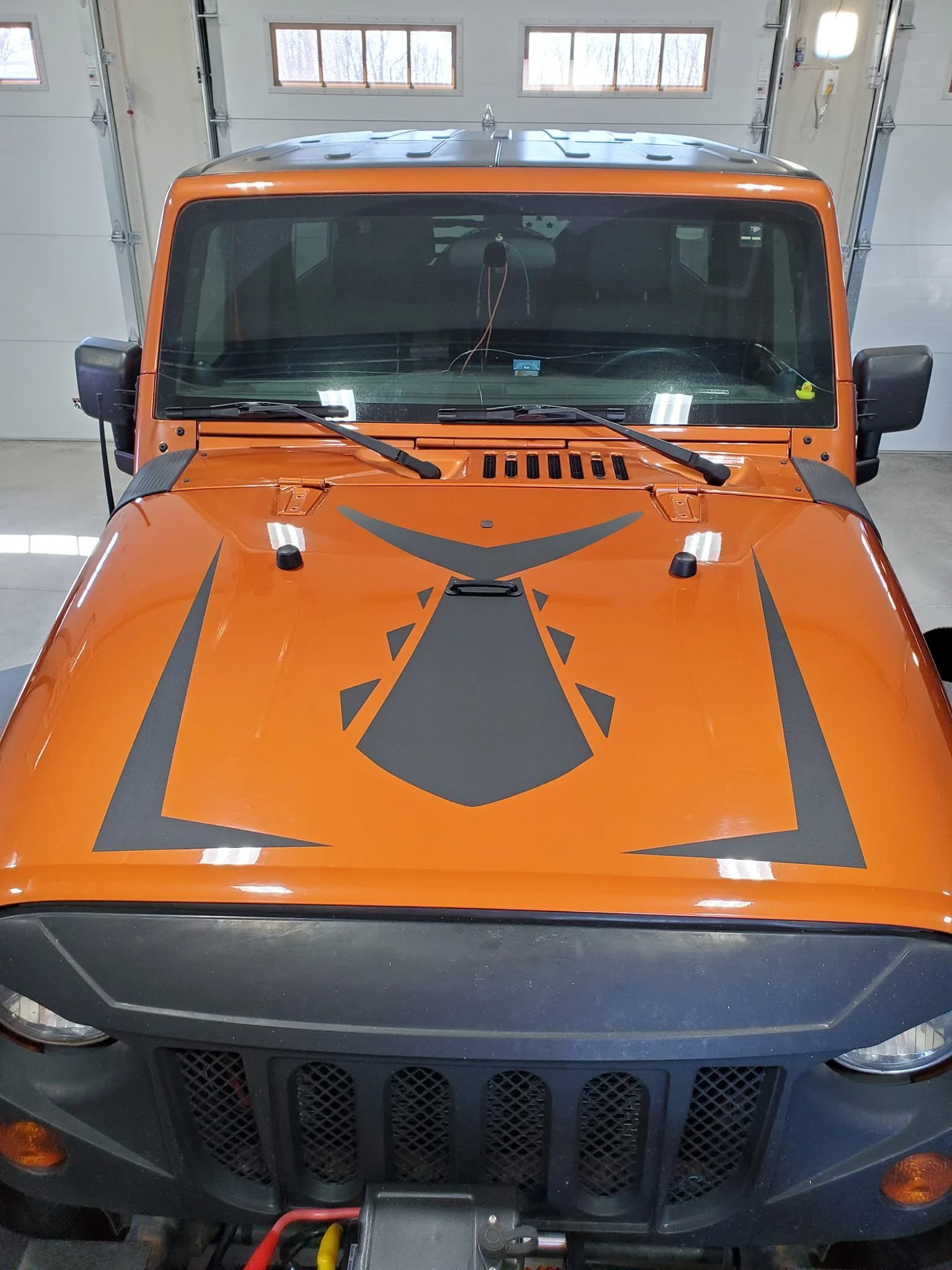 Front view of an orange Jeep SUV with black graphics on the hood, parked inside a garage.