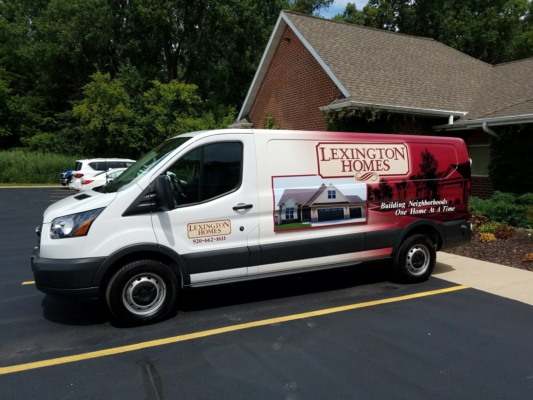Lexington Homes branded service van parked in a parking lot near a brick building and green trees, with branding and slogan for building neighborhoods.