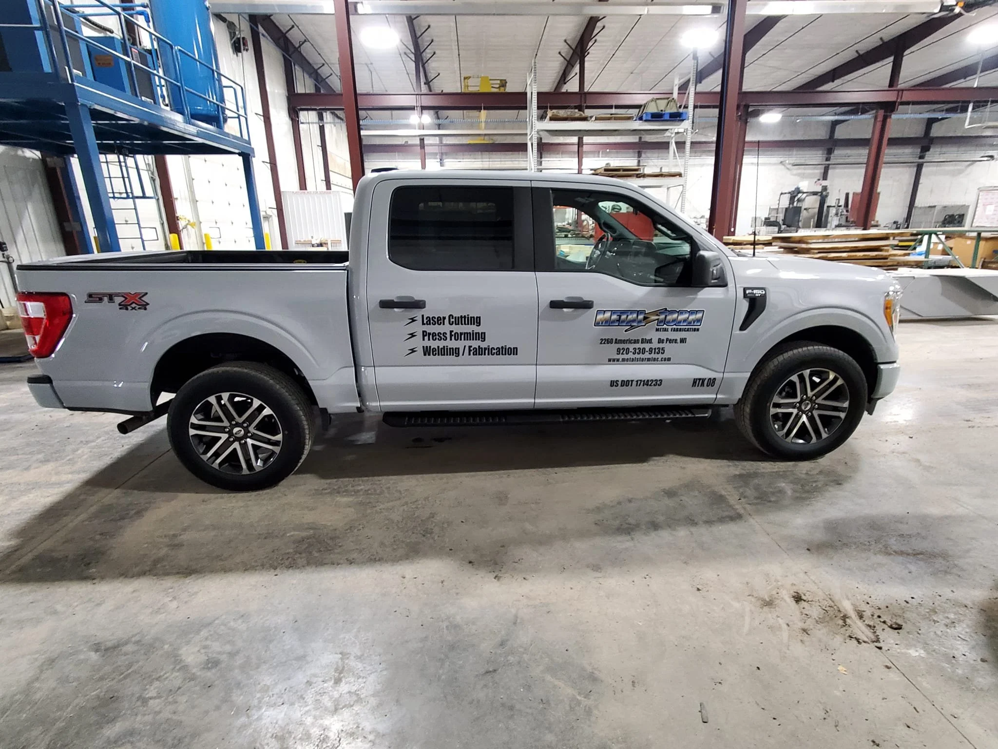 A gray pickup truck parked inside a warehouse with signage on the side advertising laser cutting, press forming, welding, and fabrication services.