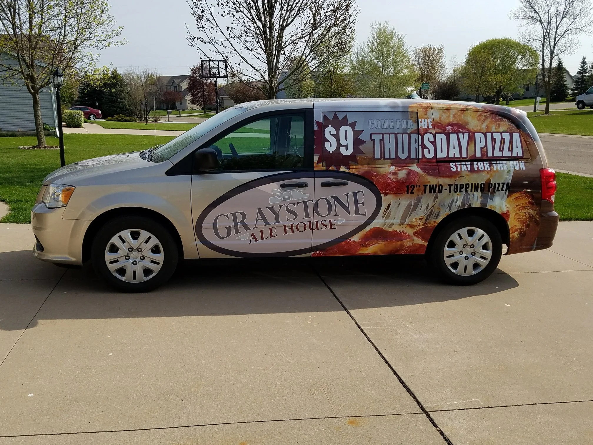A minivan with a large advertisement for Graystone Ale House on its side, promoting a $9 Thursday pizza deal, featuring images of pizza and the Graystone Ale House logo.