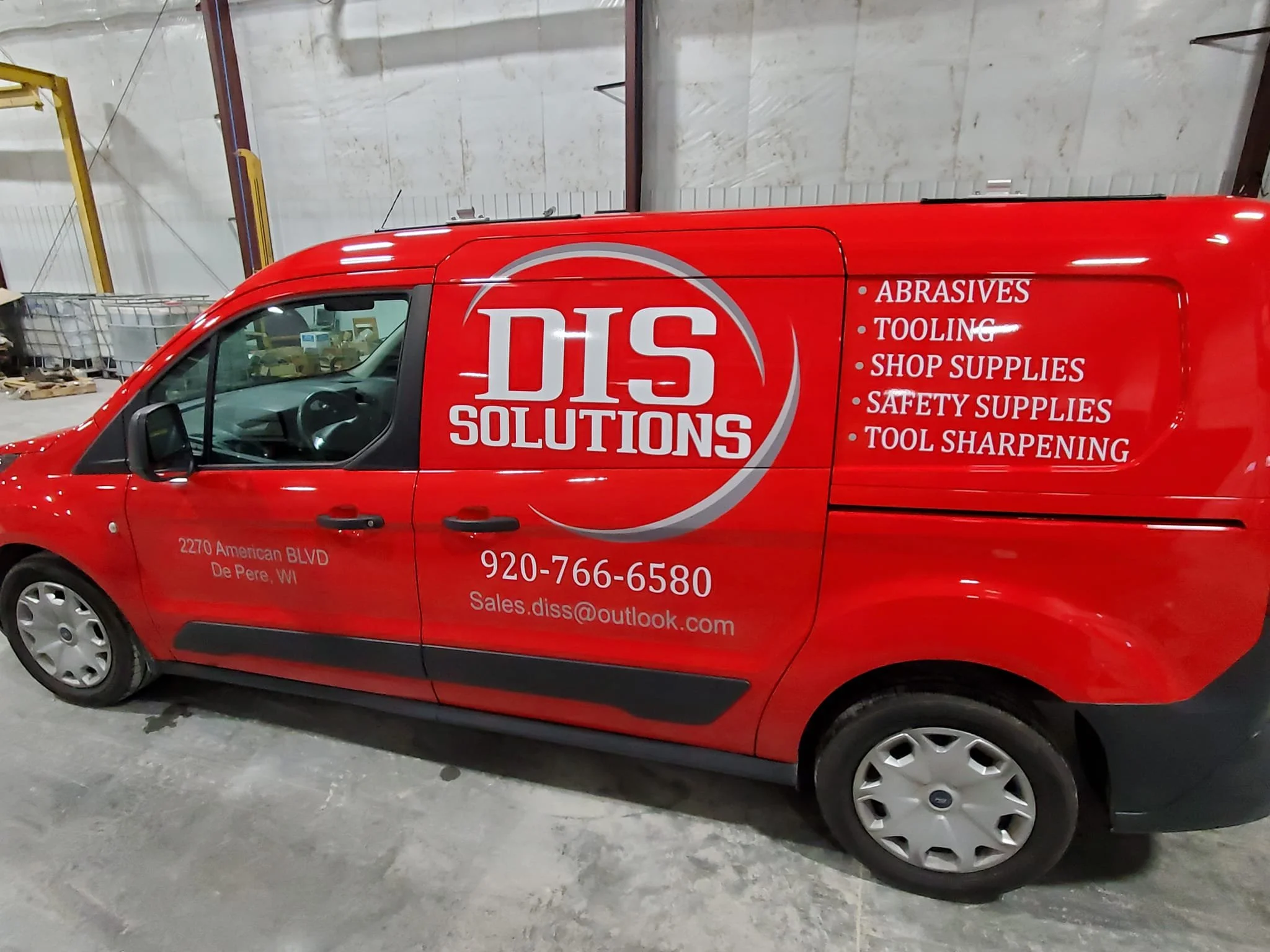 Red company van with logo and business information for DISS Solutions, listing services like abrasives, tooling, shop supplies, safety supplies, and tool sharpening, parked indoors at warehouse or garage.