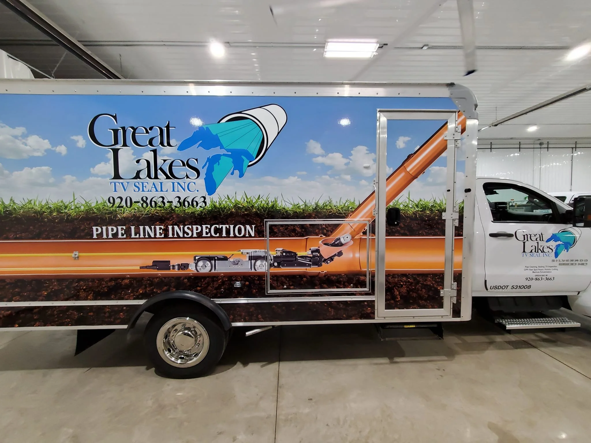 A truck with a colorful wrap advertisement for Great Lakes TV Seal Inc. showing a pipe line inspection service. The truck has a large logo of a stylized lake scene with a pipe and a mountain on a blue background.
