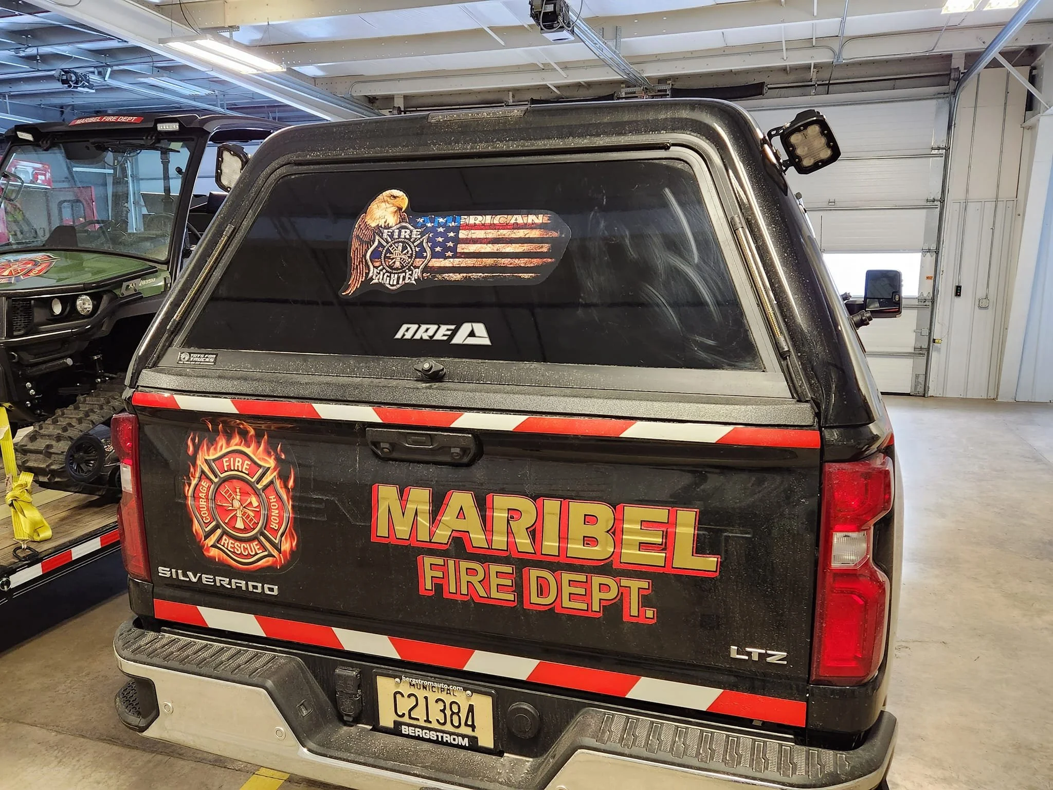 Back of a black Chevrolet Silverado pickup truck with Maribel Fire Department decals, including a fire rescue emblem and a firefighter badge with an eagle and American flag.