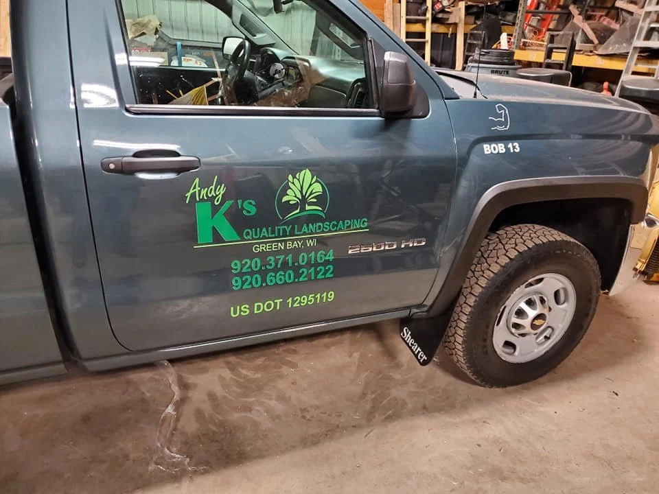 Side view of a blue pickup truck with company logo and contact information for Andy K's Quality Landscaping on the door, parked inside a garage or workshop.