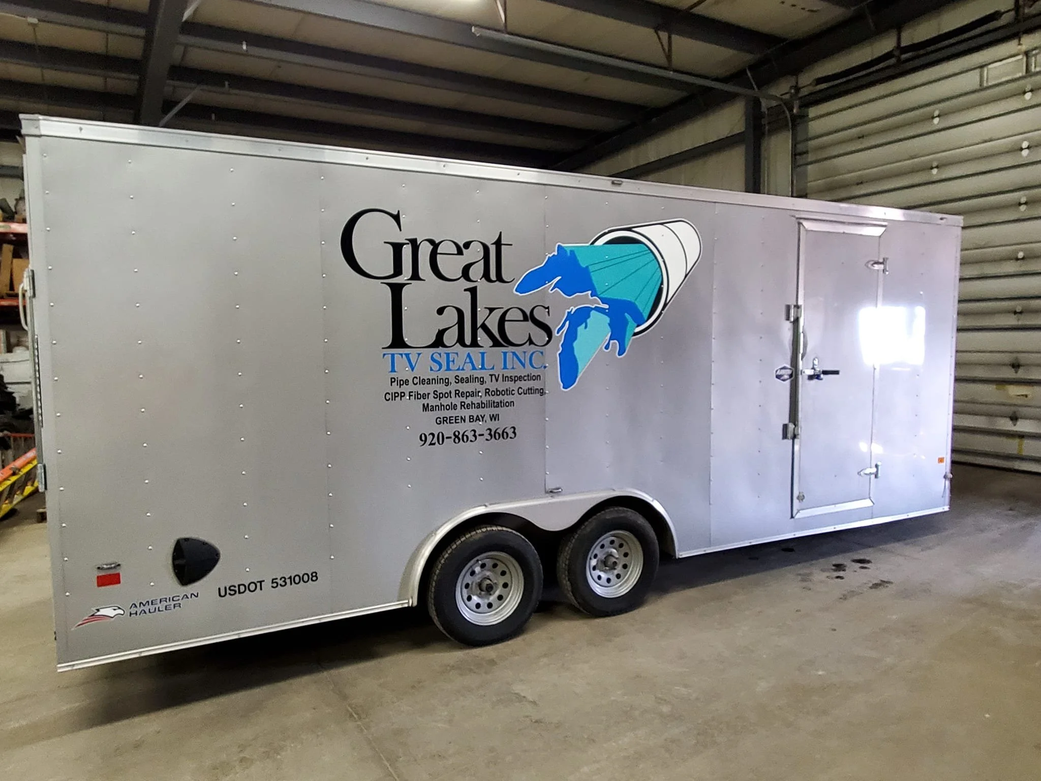 Silver enclosed trailer with business logo and contact information for Great Lakes TV Seal Inc. on the side. Logo features a blue outline of Michigan with a TV icon. Text includes services like pipe cleaning, sealing, TV inspection, and more. Locatio