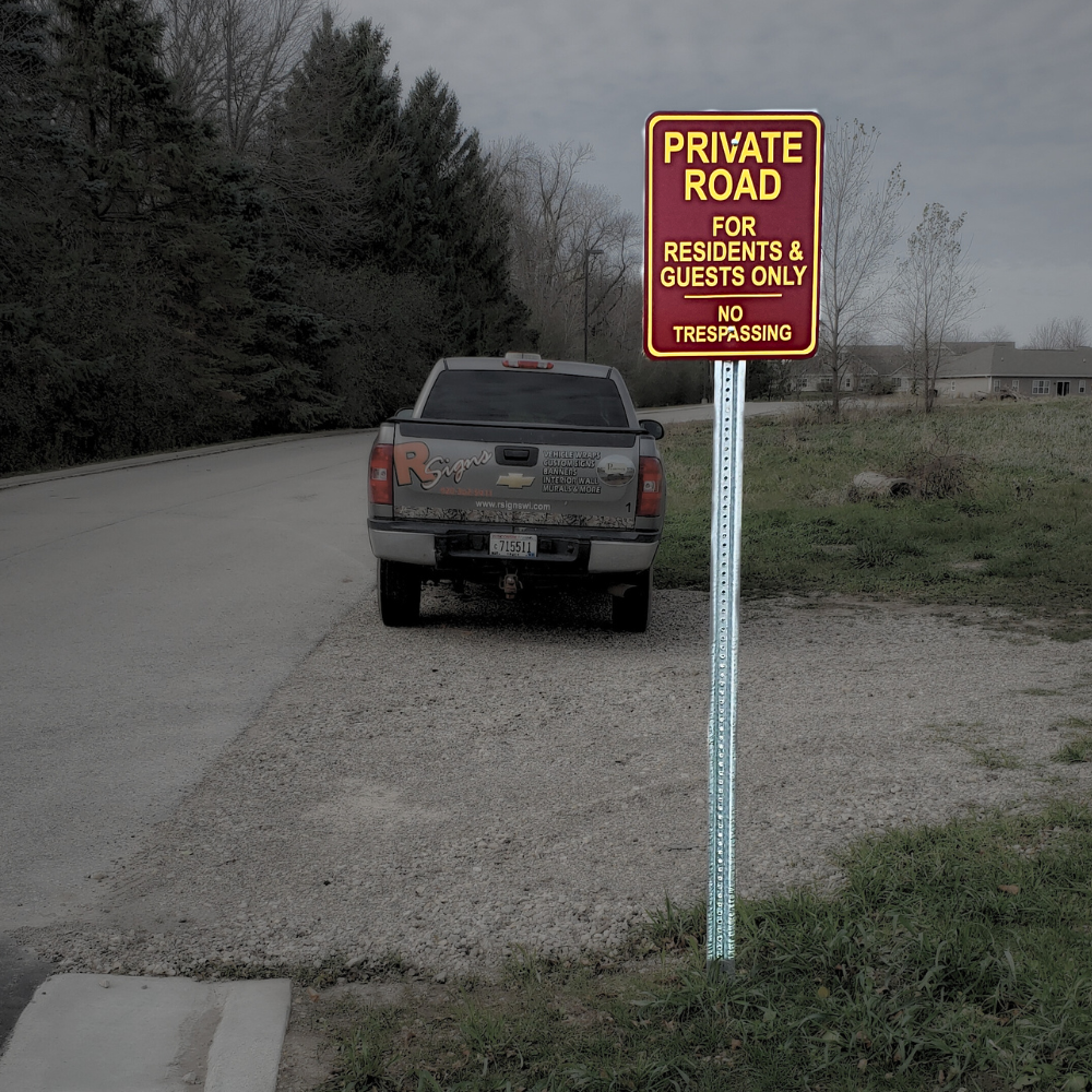 A pickup truck parked on a gravel shoulder next to a paved road with a sign that reads 'PRIVATE ROAD FOR RESIDENTS & GUESTS ONLY NO TRESPASSING'. There are trees and houses in the background under a cloudy sky.
