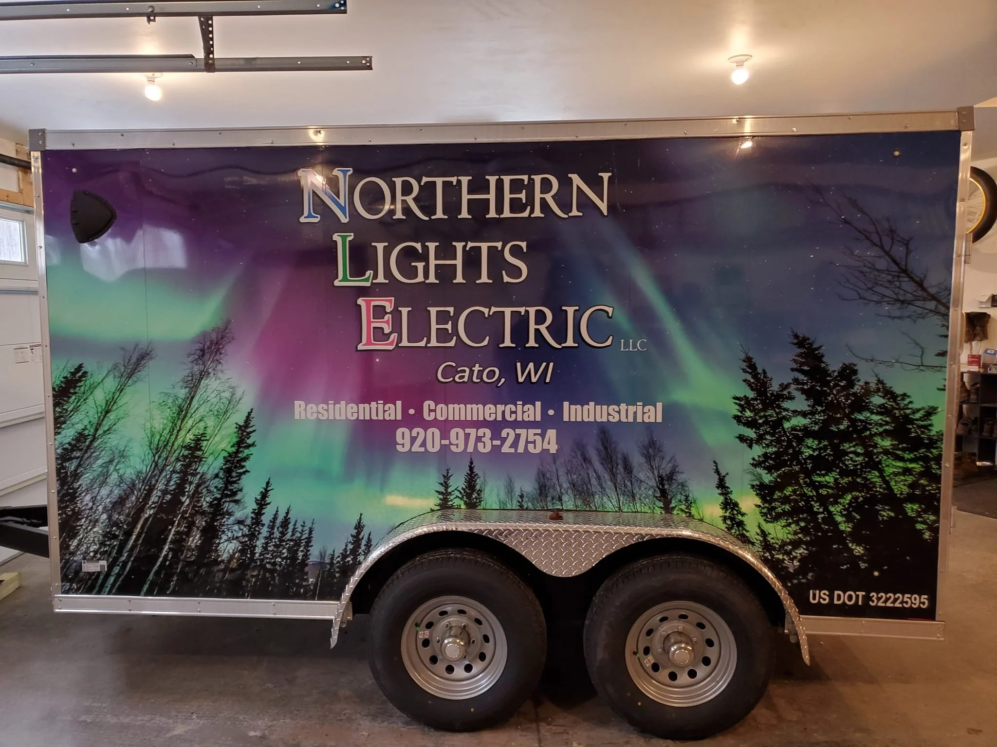 A trailer with a Northern Lights Electric LLC advertisement featuring an aurora borealis display in the sky over a silhouette of trees, with contact information and business details.