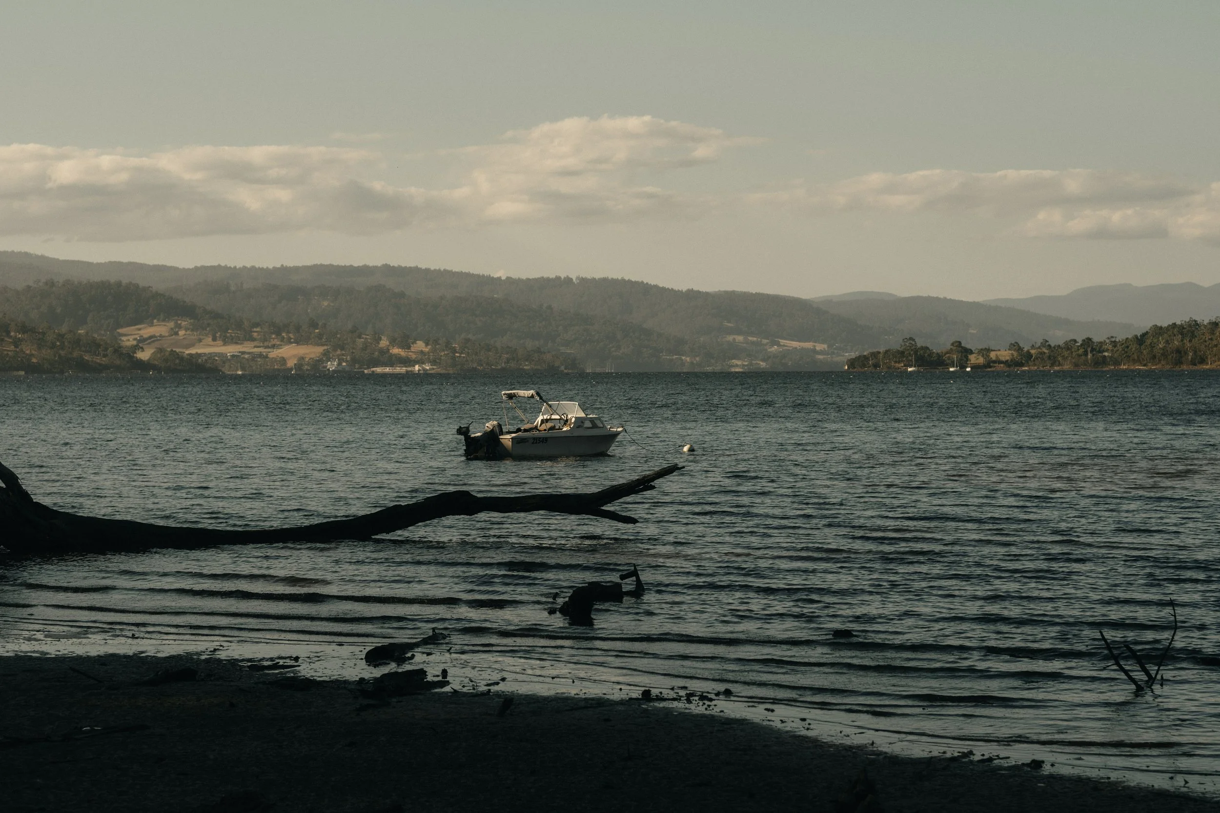 A boat floating on a lake with distant hills and a partly cloudy sky in the background.
