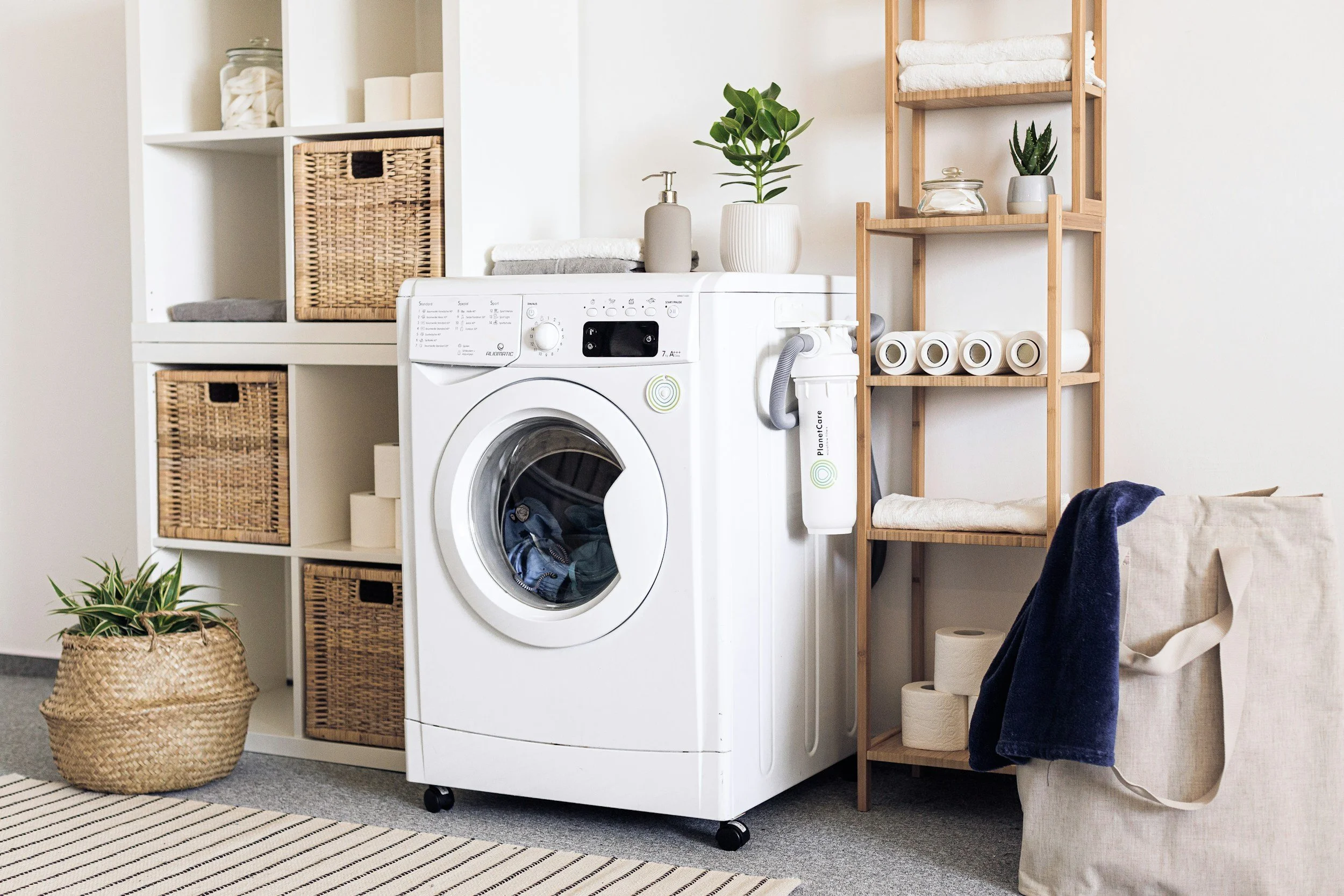 Laundry room with a washing machine, shelves with towels and plants, and storage baskets.