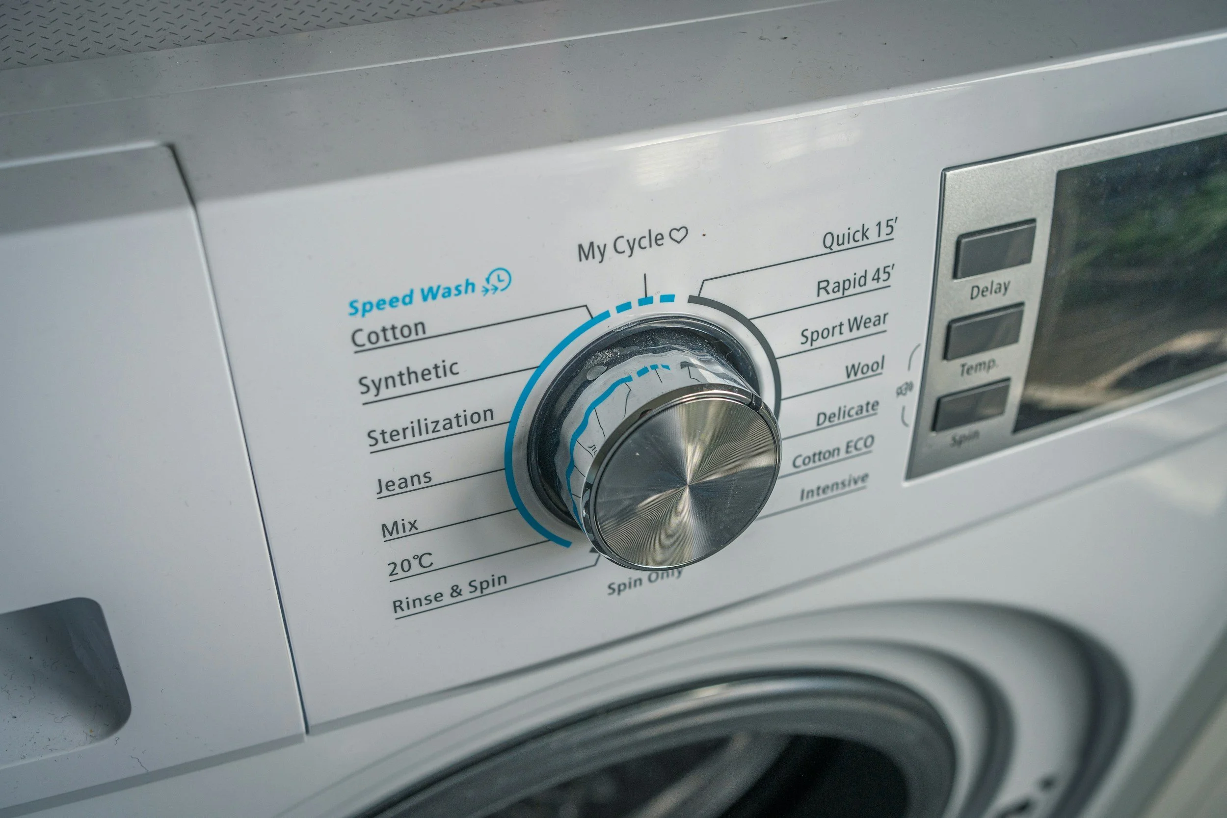 Close-up of a washing machine control panel with cycle options like Cotton, Synthetic, Jeans, and spin, and a large central dial.