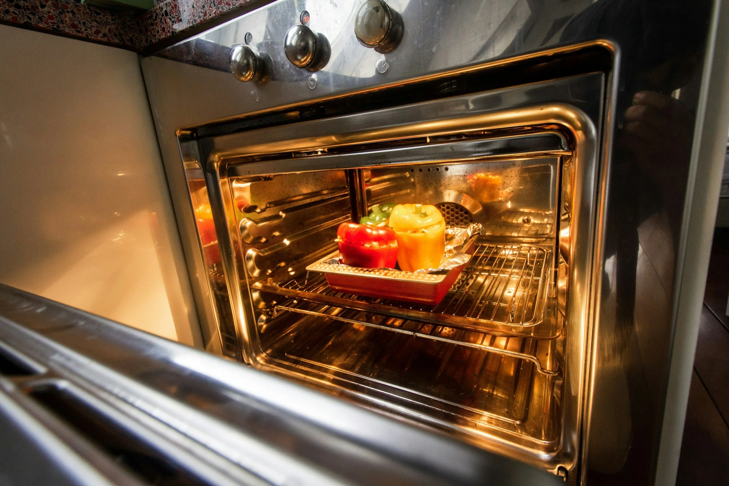 An oven with colorful bell peppers inside, viewed through the open door.