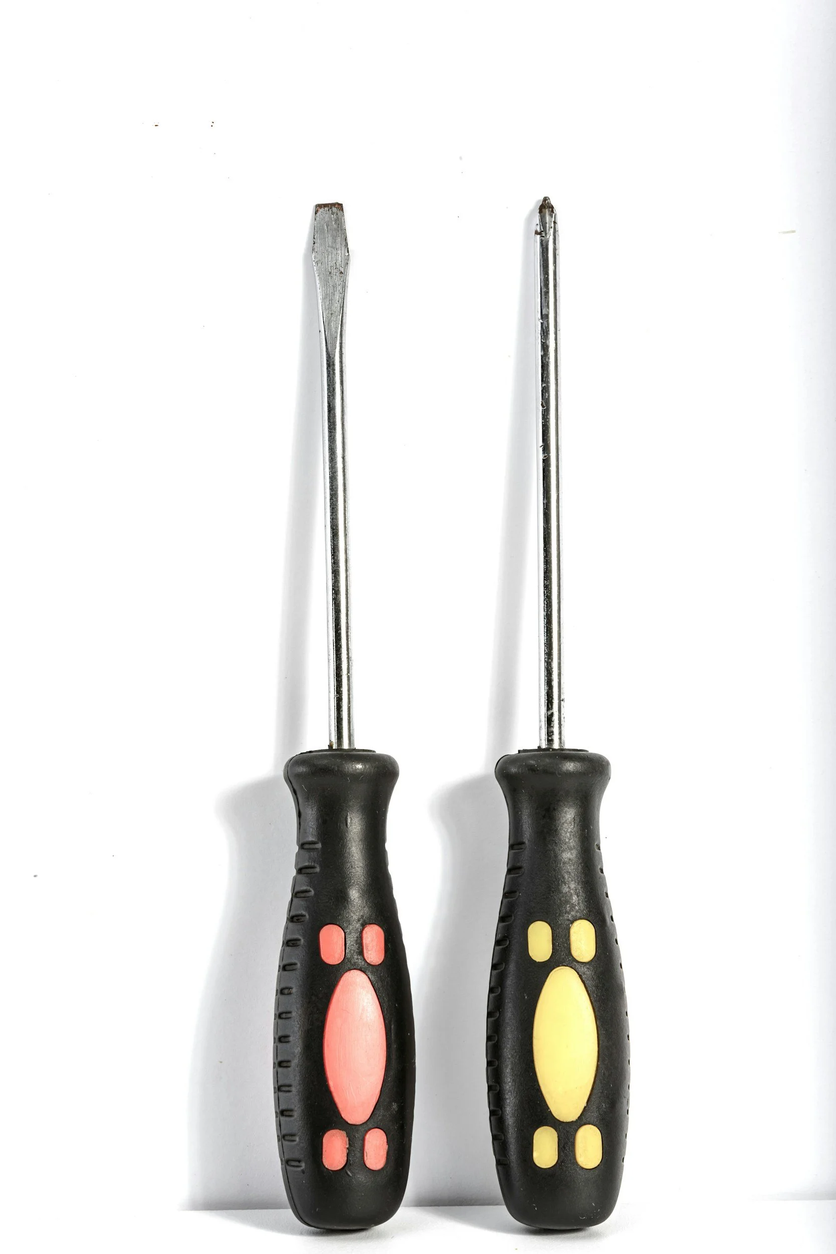 Two screwdrivers with black handles and red and yellow accents, placed on a white surface.