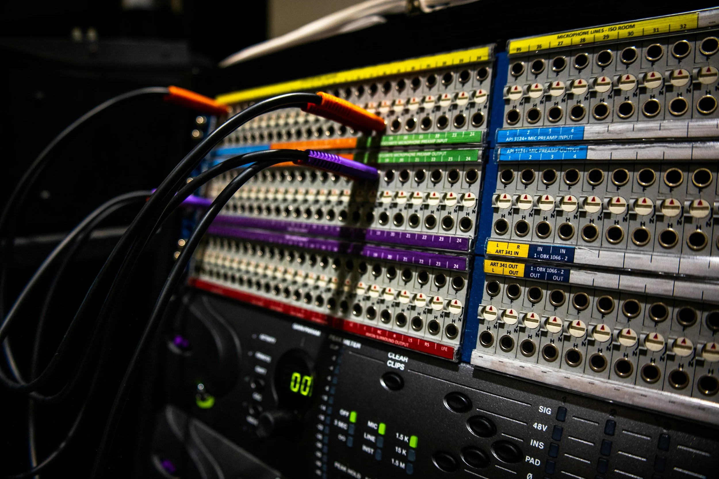 Close-up of an audio mixing console with various colorful labeled connections and knobs.
