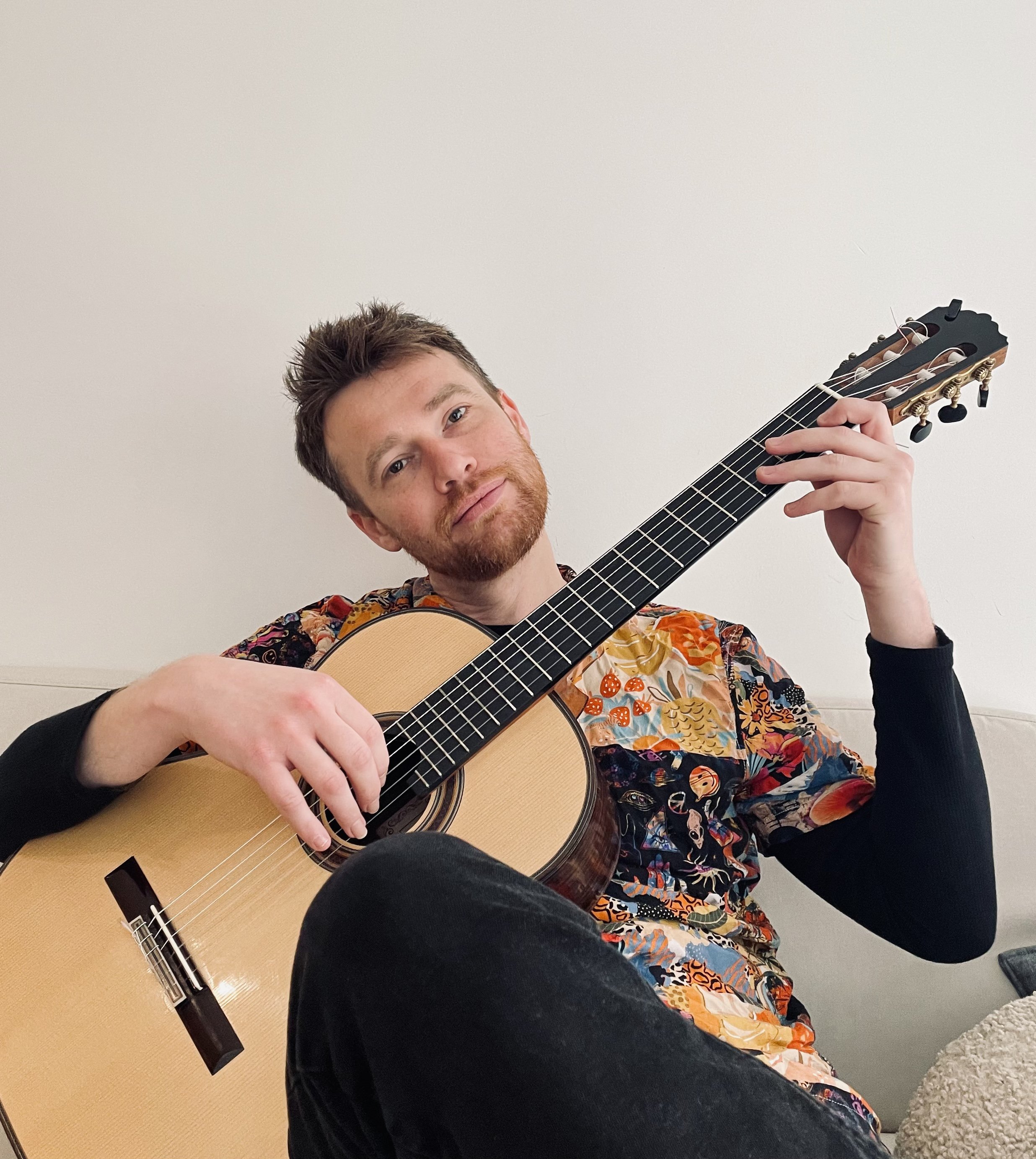 A man sitting on a sofa playing an acoustic guitar.