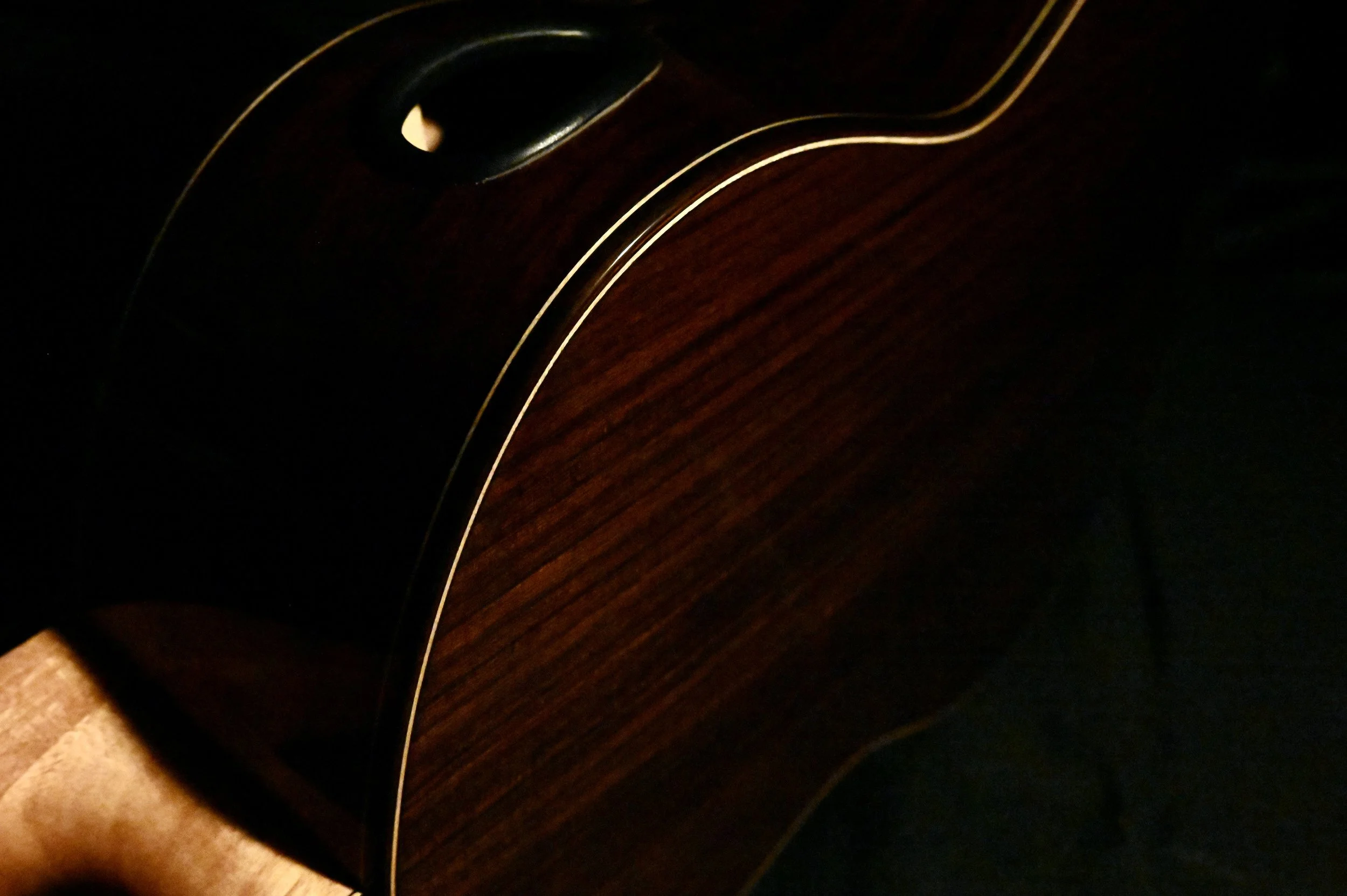 Close-up of an acoustic guitar highlighting its dark wooden body, with a focus on the curved side and a small part of the sound hole.