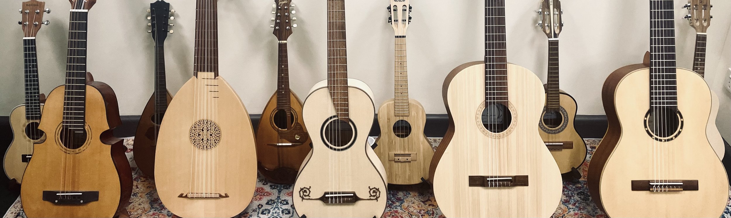 A collection of various acoustic and classical guitars arranged on a patterned rug against a plain wall.