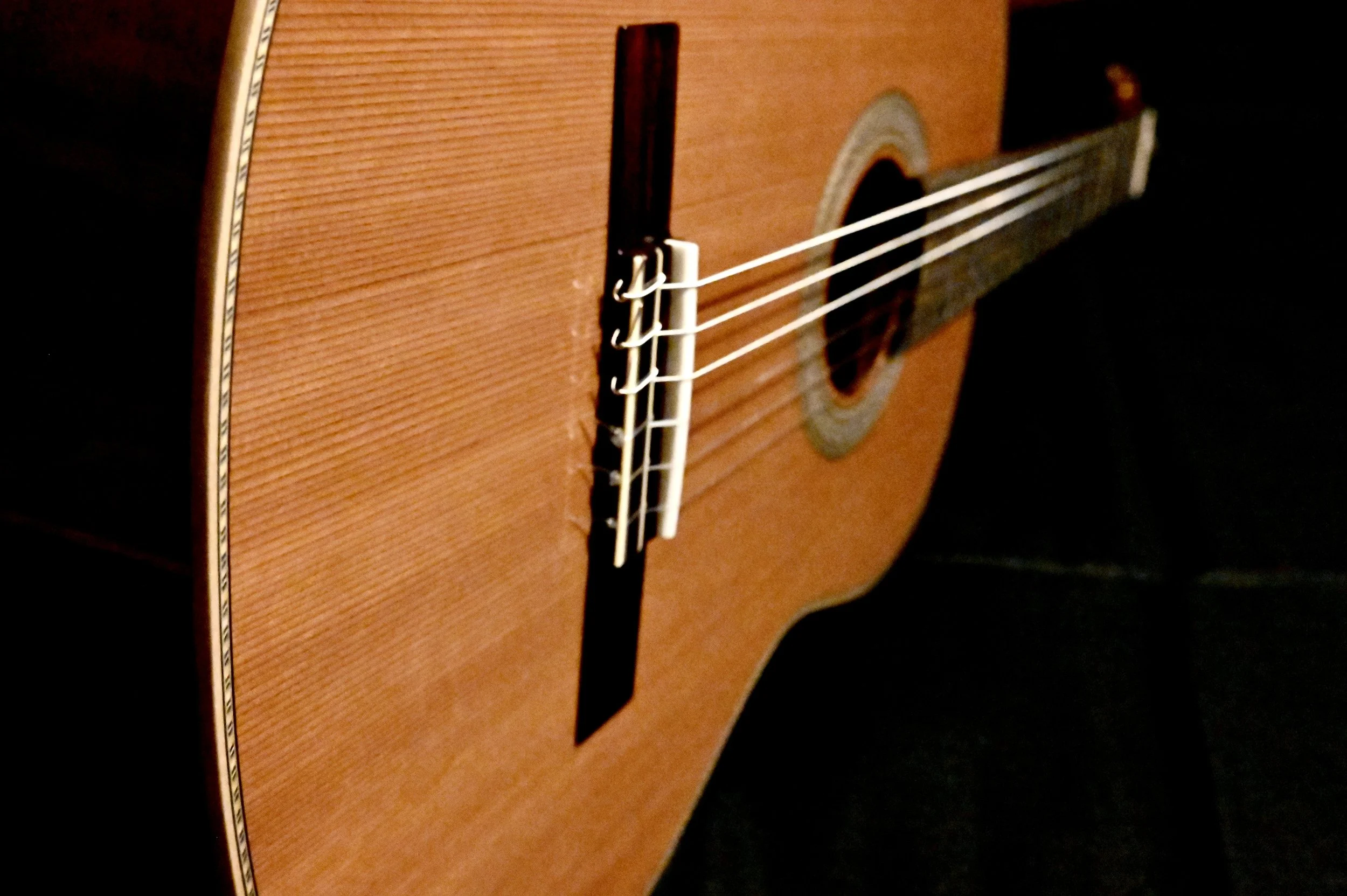 Close-up of an acoustic guitar focusing on the body, strings, and bridge, with a dark background.