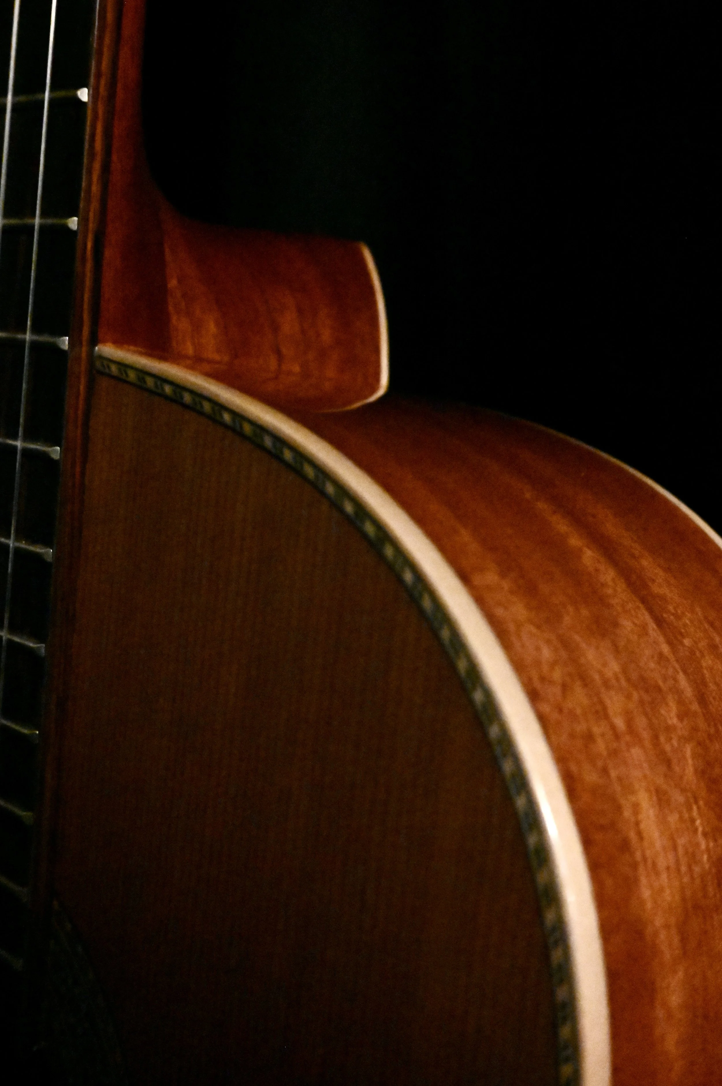 Close-up of a vintage acoustic guitar showcasing the curve of the body and part of the neck with strings, against a dark background.