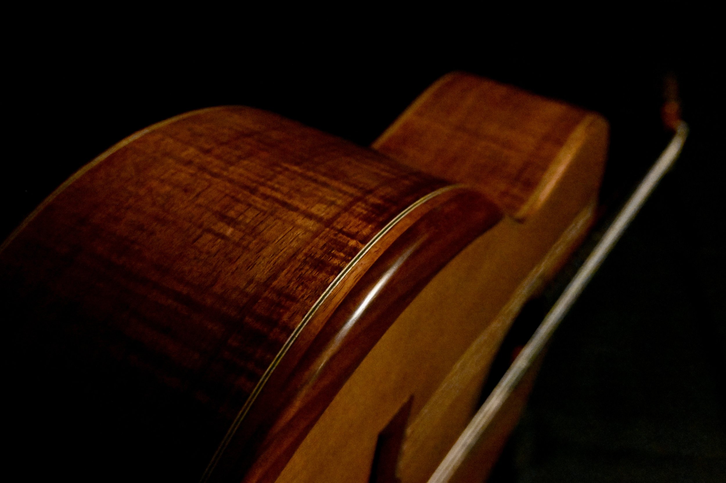 Close-up of the back of a wooden acoustic guitar against a dark background.