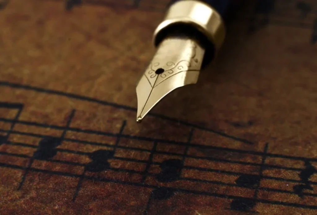 Close-up of a gold fountain pen tip on a sheet of musical staff paper with musical notes.