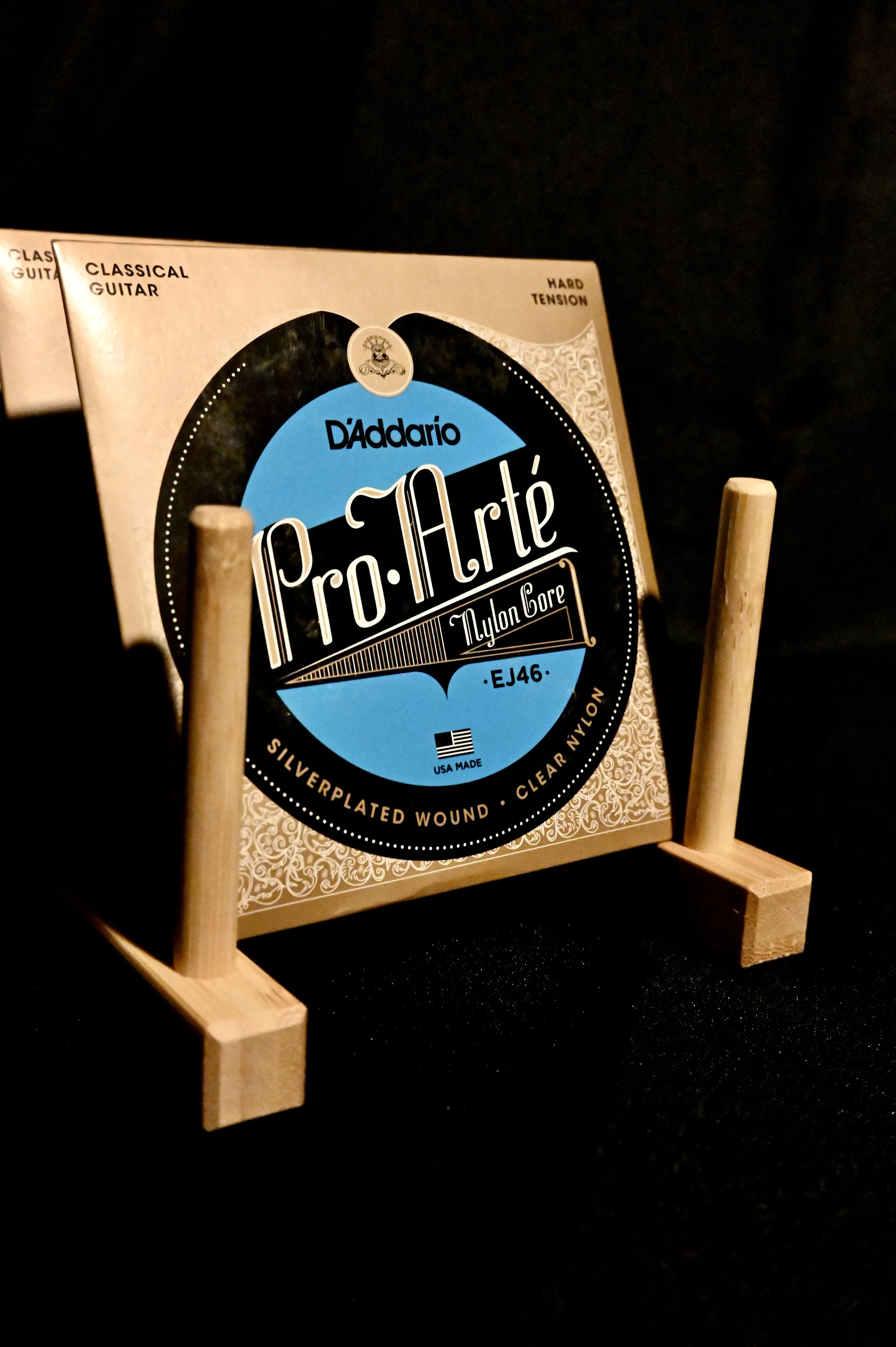 A package of D'Addario Pro-Arte nylon core classical guitar strings held upright on a small wooden stand against a black background.