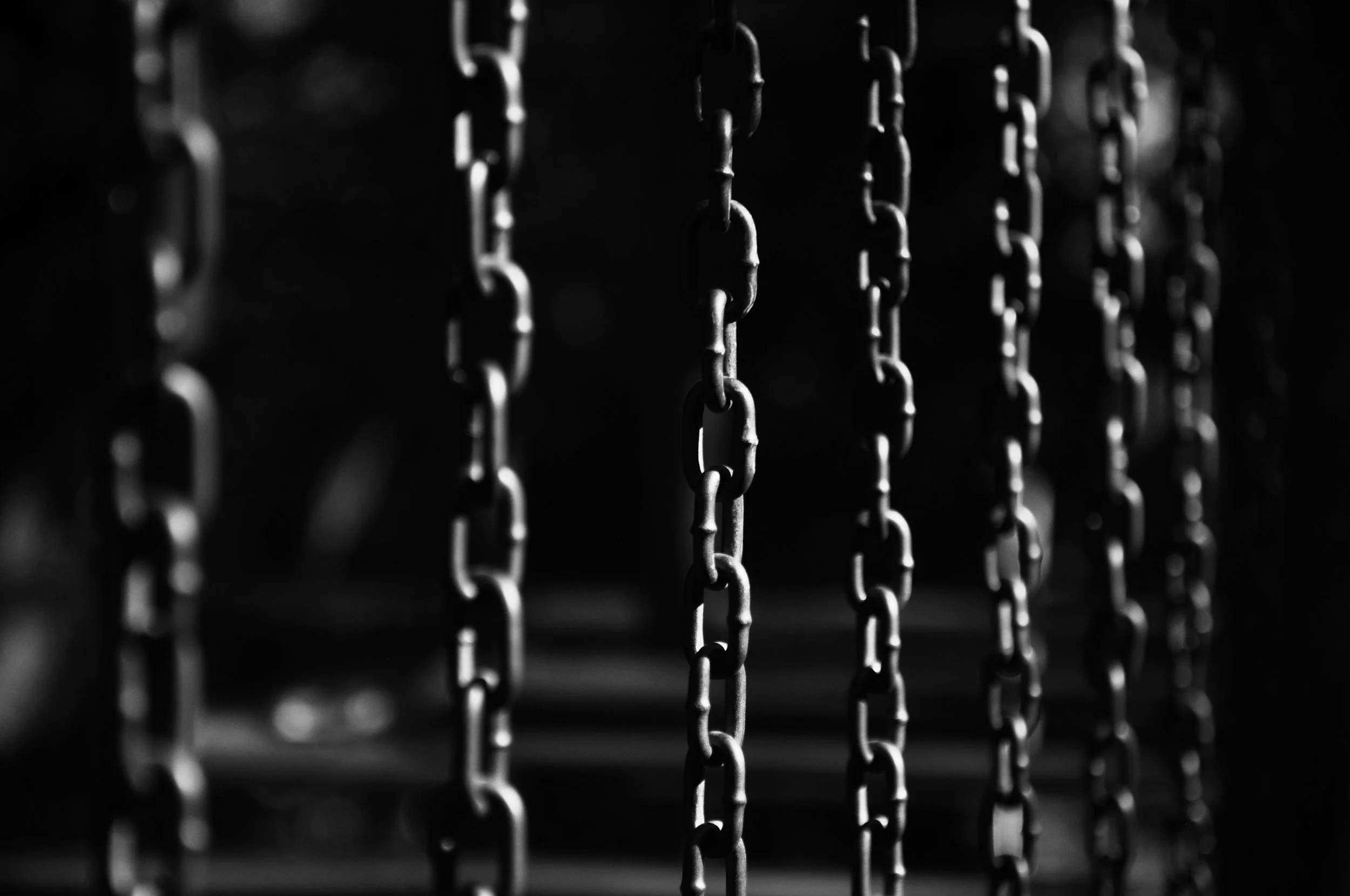 Black and white photo of hanging metal chains with focus on the middle chain, dark background.