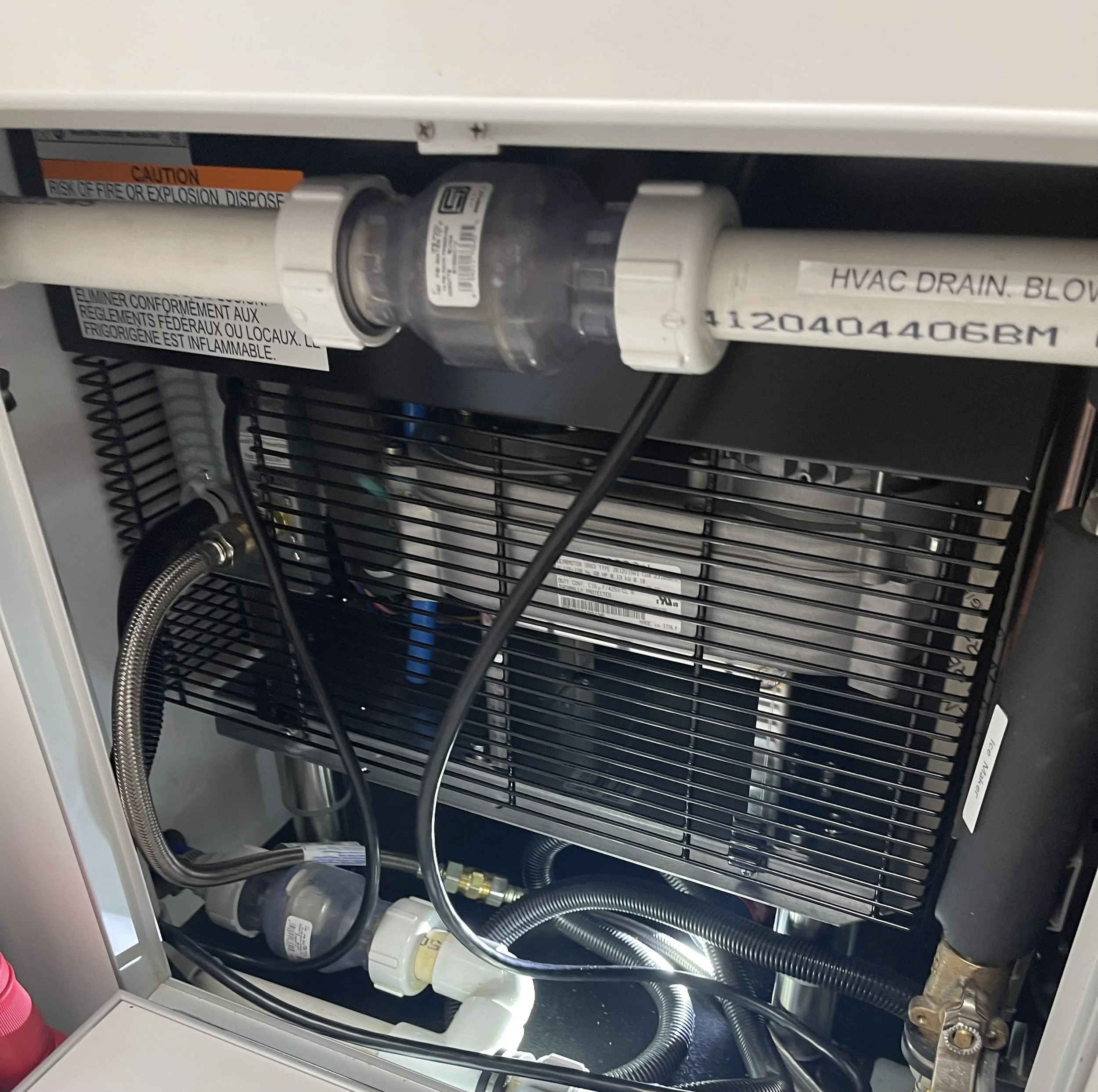 Inside view of an HVAC or refrigeration unit showing pipes, hoses, and a metal cooling coil.
