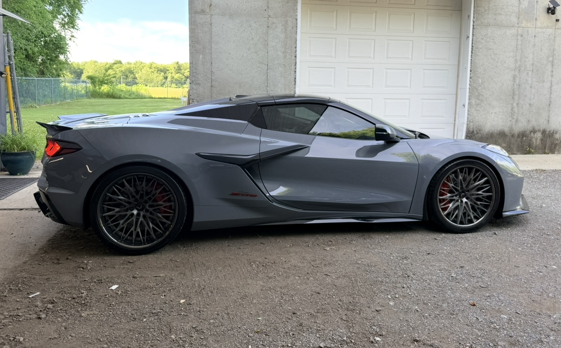 Gray sports car parked in front of a garage with green trees in the background.