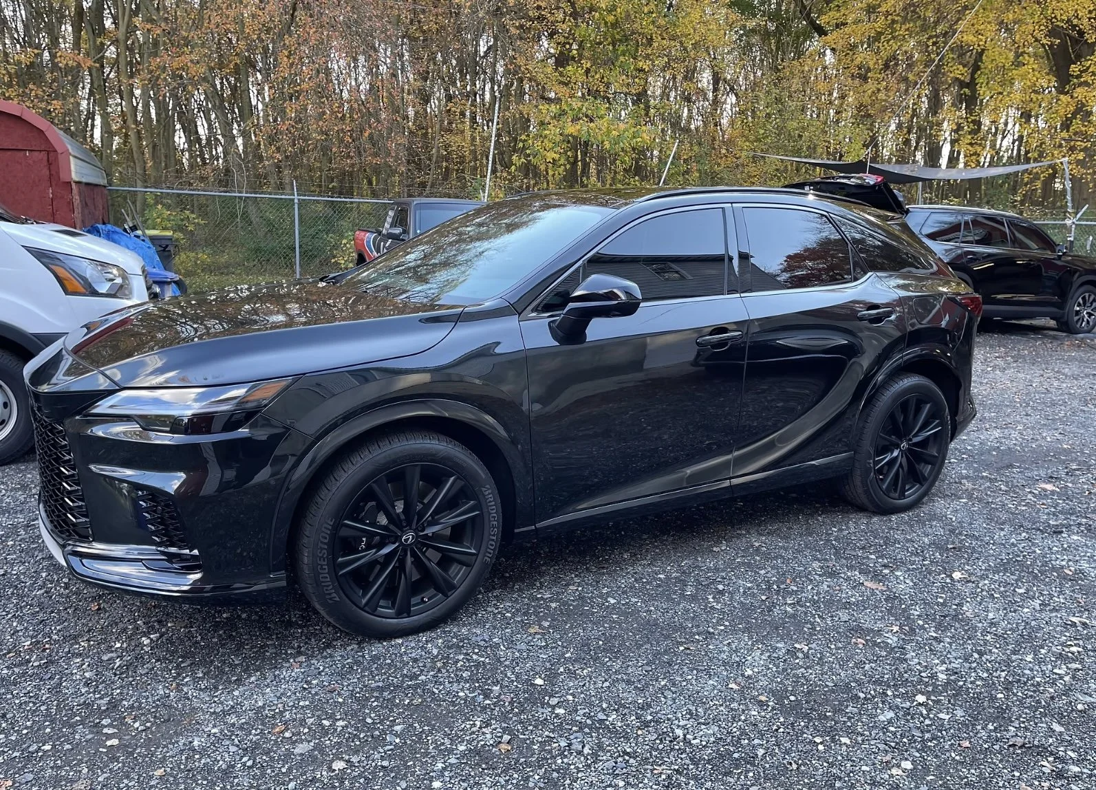 A black luxury SUV parked on a gravel lot, with trees and other cars in the background.