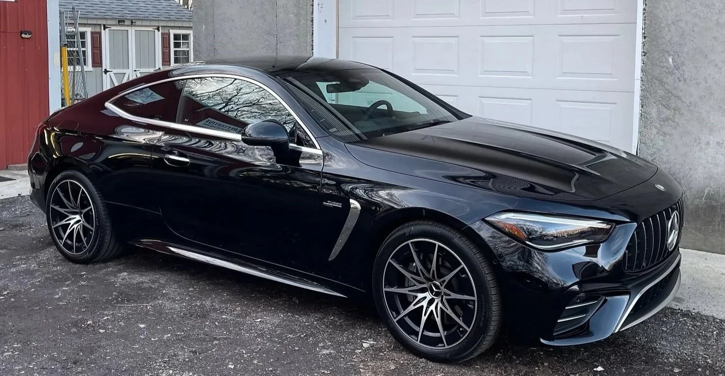 A black Mercedes-Benz coupe parked on a gravel driveway in front of a white garage door and a red shed.