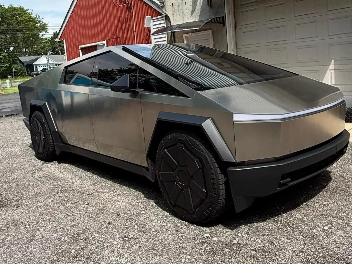 A futuristic silver electric Tesla CyberTruck parked outside on a gravel driveway.