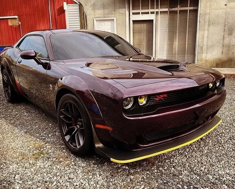 Black Dodge Challenger with yellow accents parked on gravel outside a building.