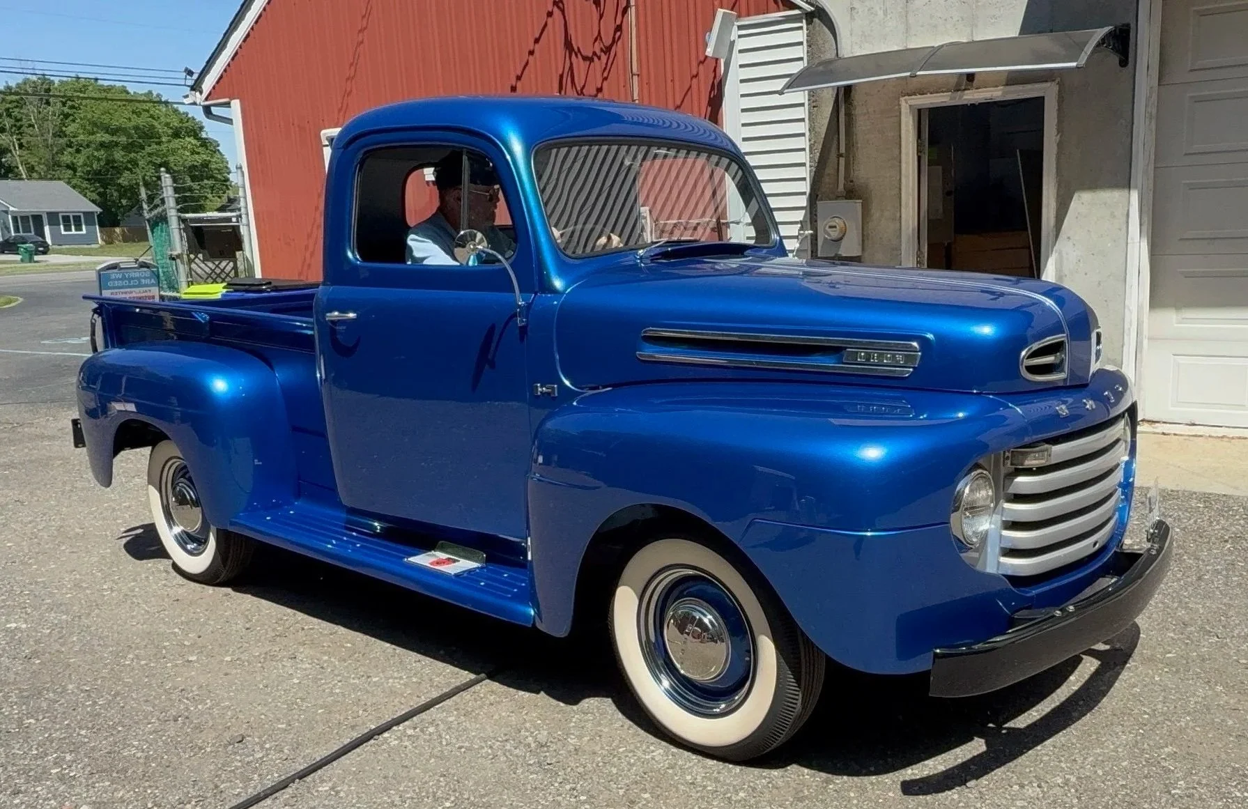 A vintage blue pickup truck with whitewall tires parked outside near a building with a red wall and a garage door.