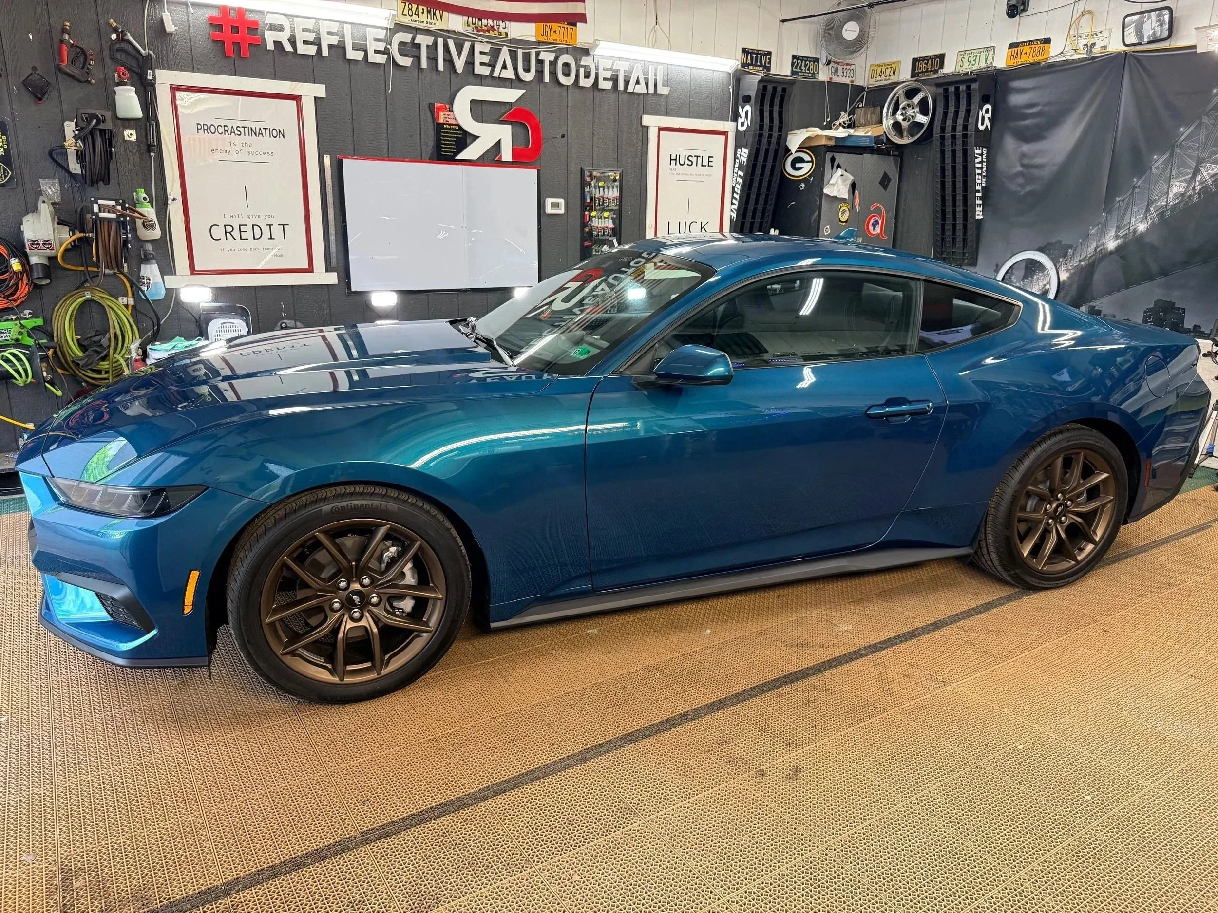 A blue sports car parked inside a garage with wall decorations, signs, and tools.