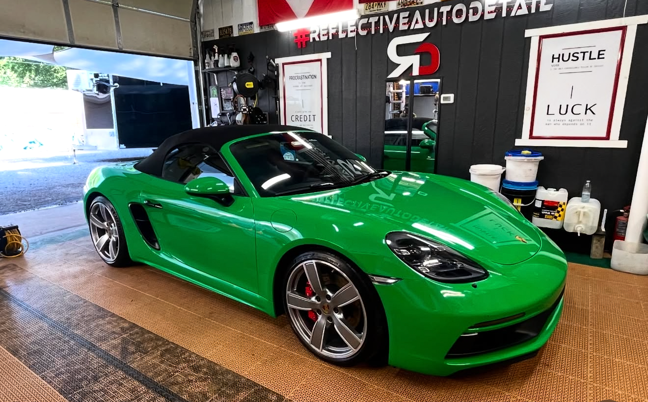 Green sports car with black roof inside a garage with posters and equipment on the walls.