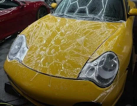 Yellow sports car covered in soap suds during a wash, with soap foam on the windshield and hood.