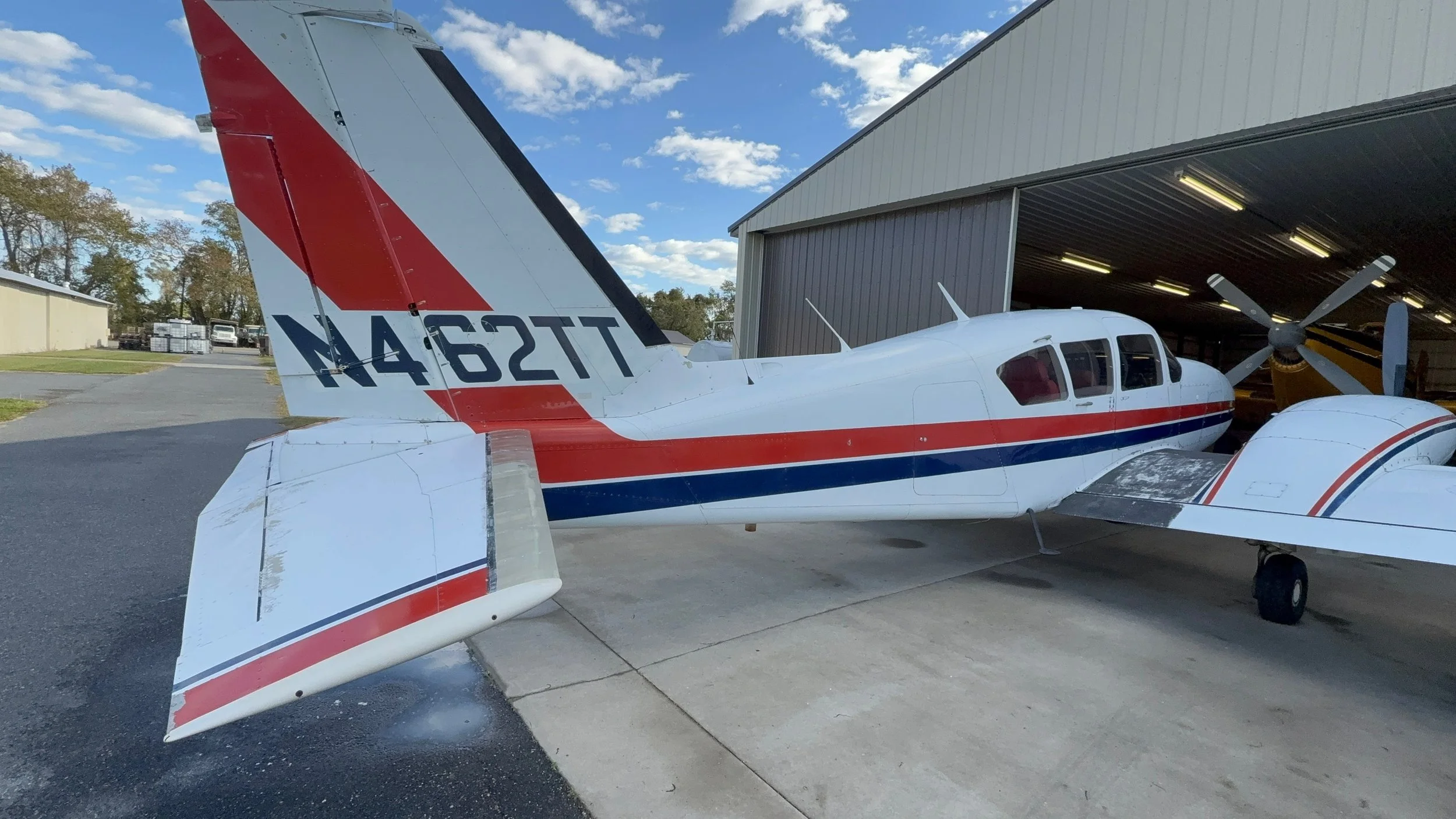 Small white aircraft with red and blue stripes parked inside a hangar on a clear day.