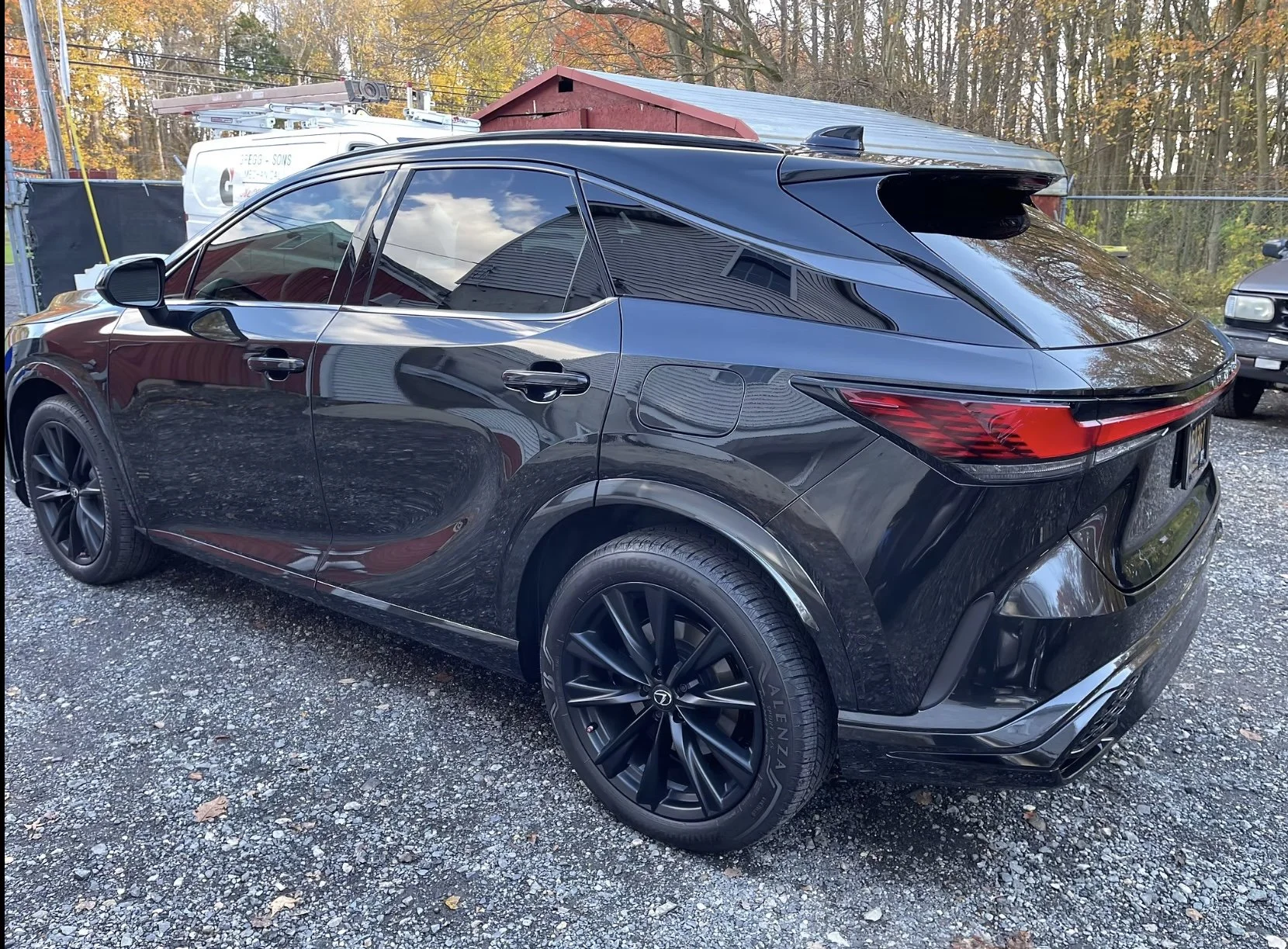 A black luxury SUV parked on a gravel lot with autumn trees in the background.