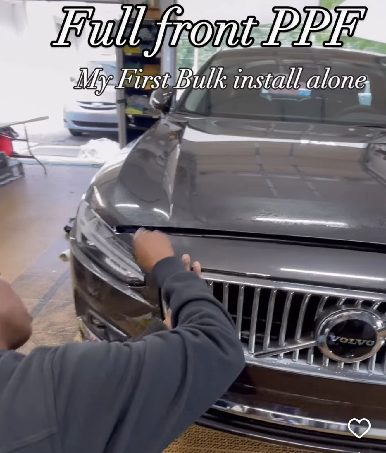 Person installing a full front aftermarket vehicle paint protection film (PPF) on a black luxury car in a garage.